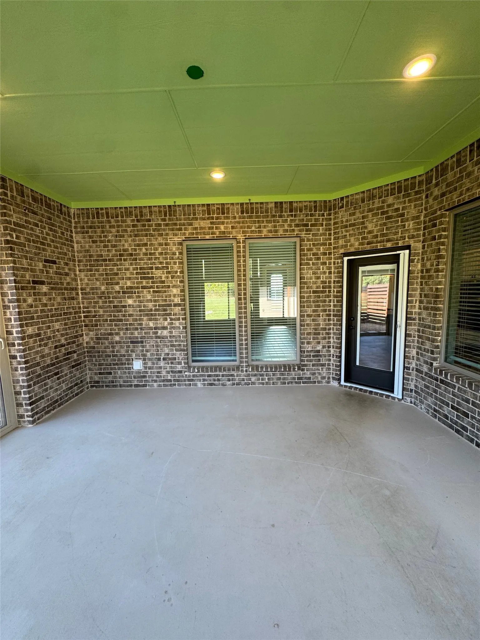 Covered patio featuring a brick exterior, concrete flooring, recessed lighting, and multiple windows with blinds
