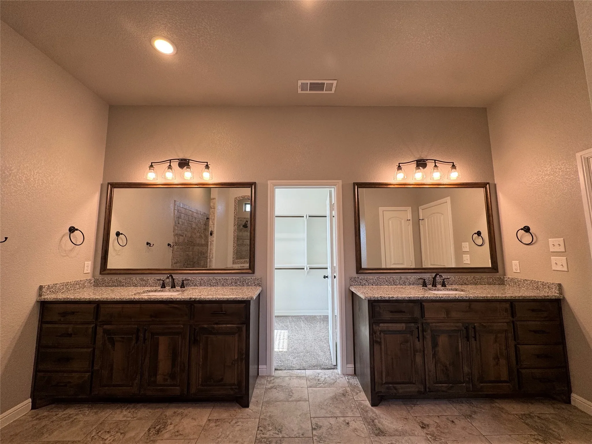 Dual wood-finish vanities each with a single basin, stone-finish countertops, and framed mirrors