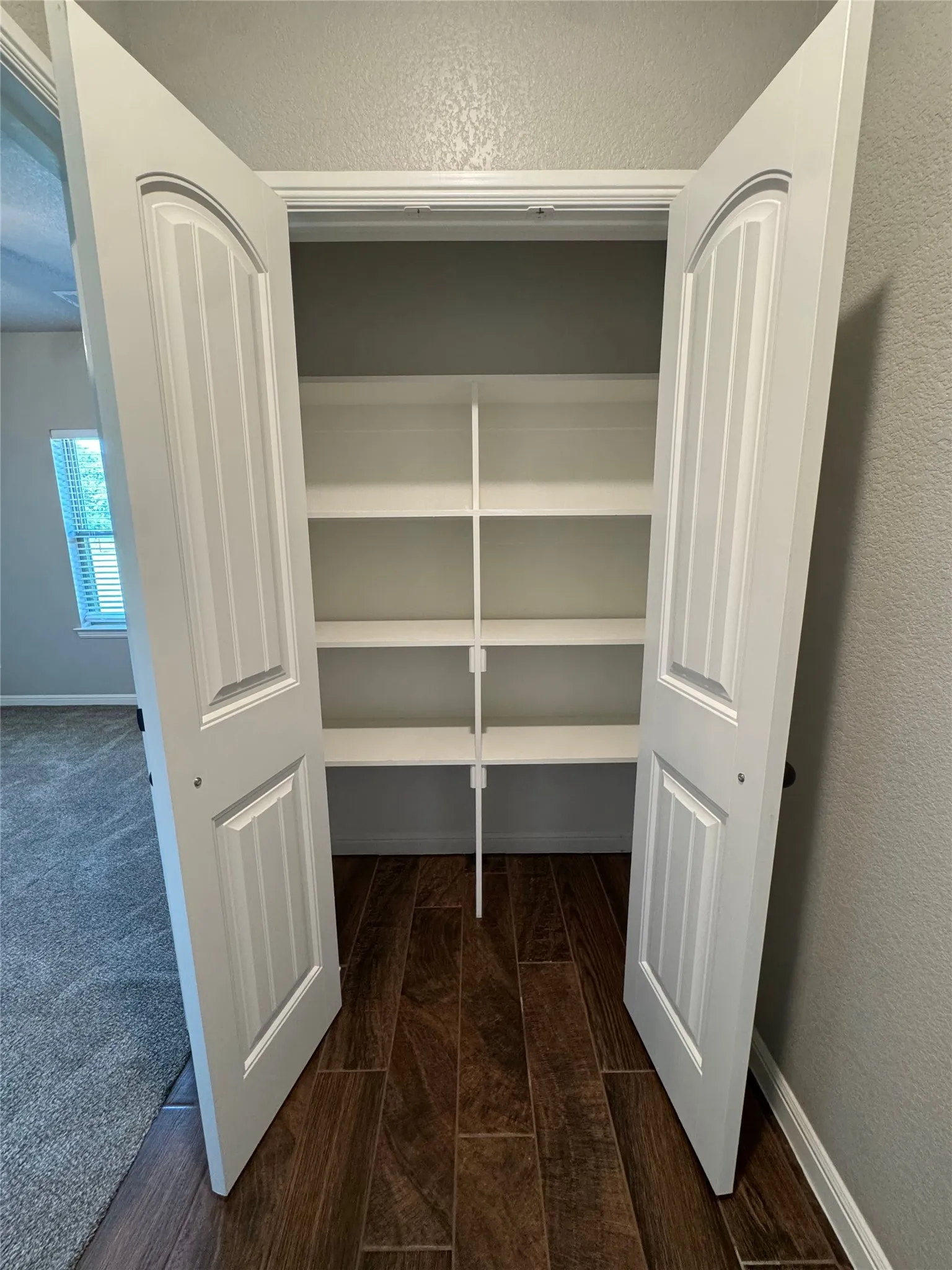 White bi-fold doors opening to built-in shelving, featuring wood-finish flooring