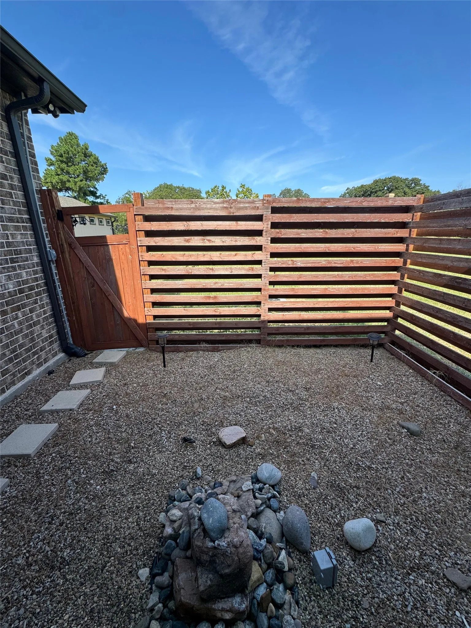 Private outdoor space featuring wood fencing, a stone water feature, gravel ground cover, and stepping stones