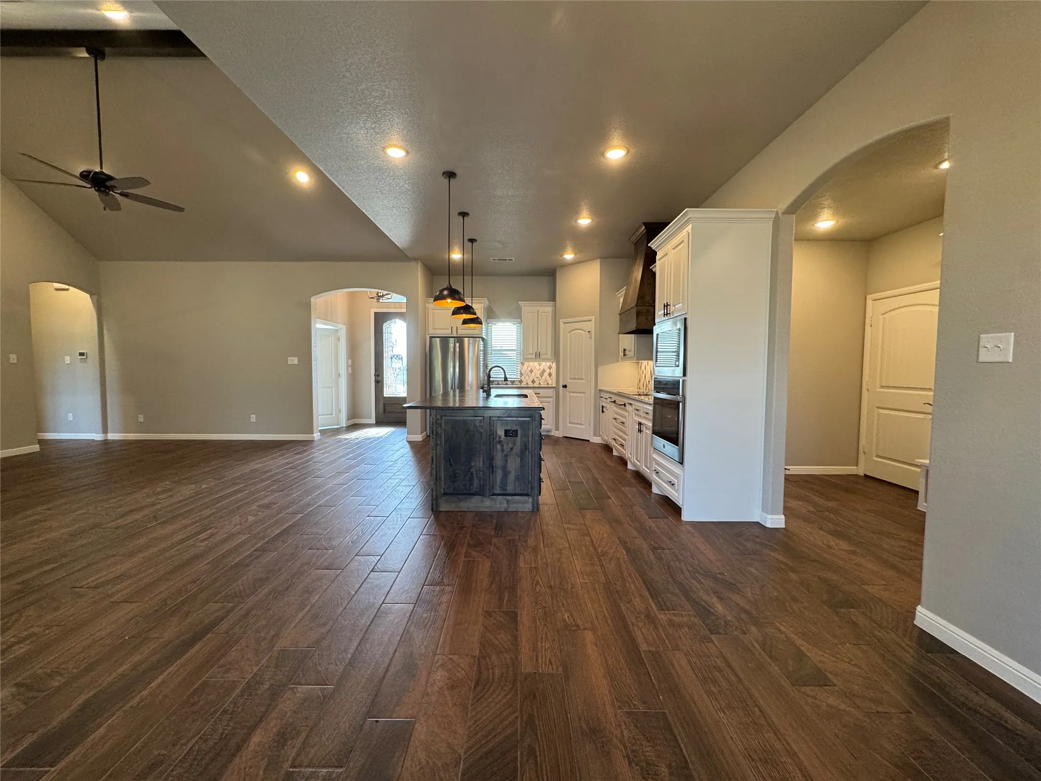Open-concept living space featuring wood-finish flooring, vaulted ceilings, recessed lighting, and a modern kitchen island with pendant lighting