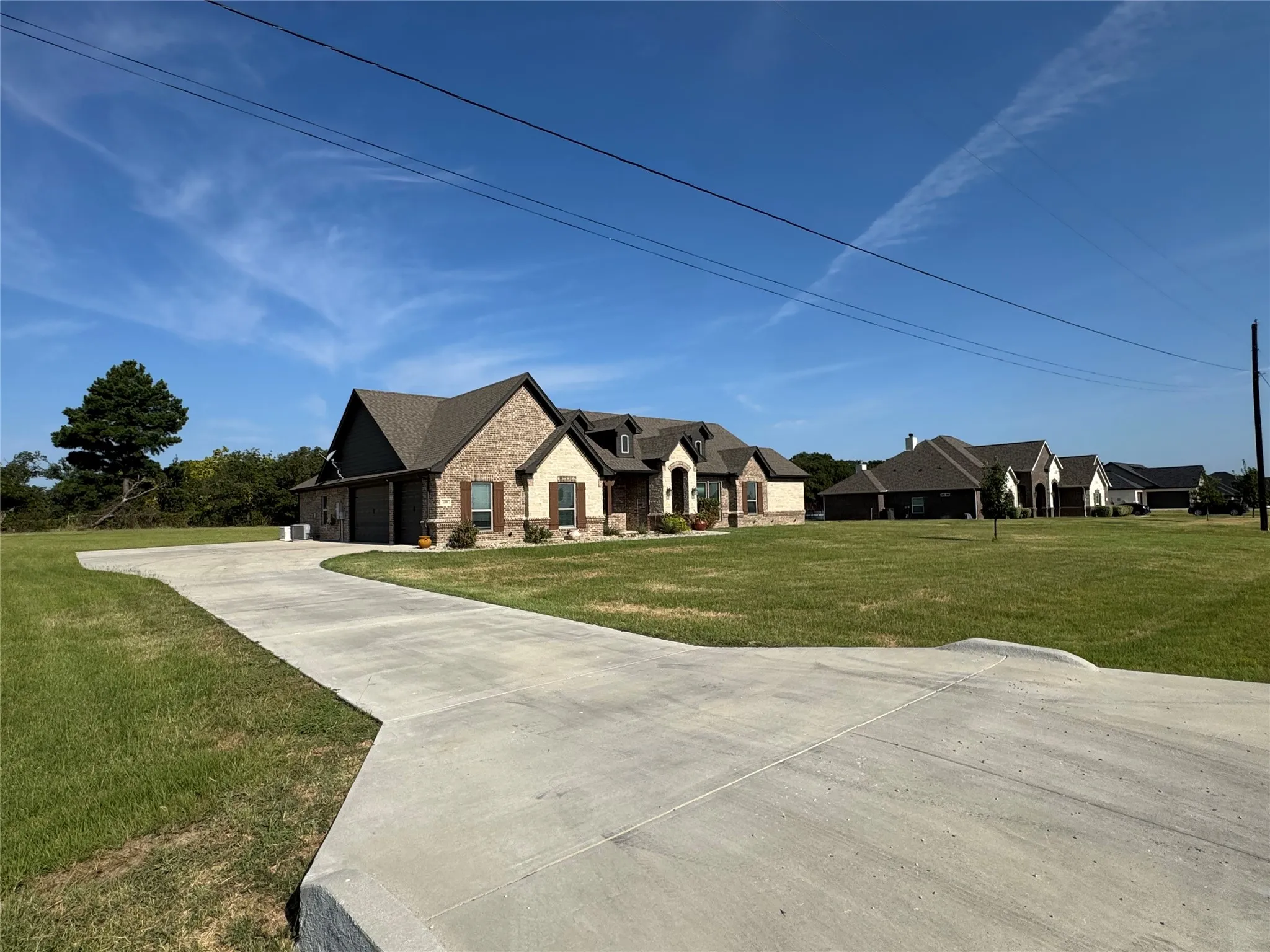 Exterior featuring brick and siding facade, gabled roofing, a concrete driveway, and a manicured lawn