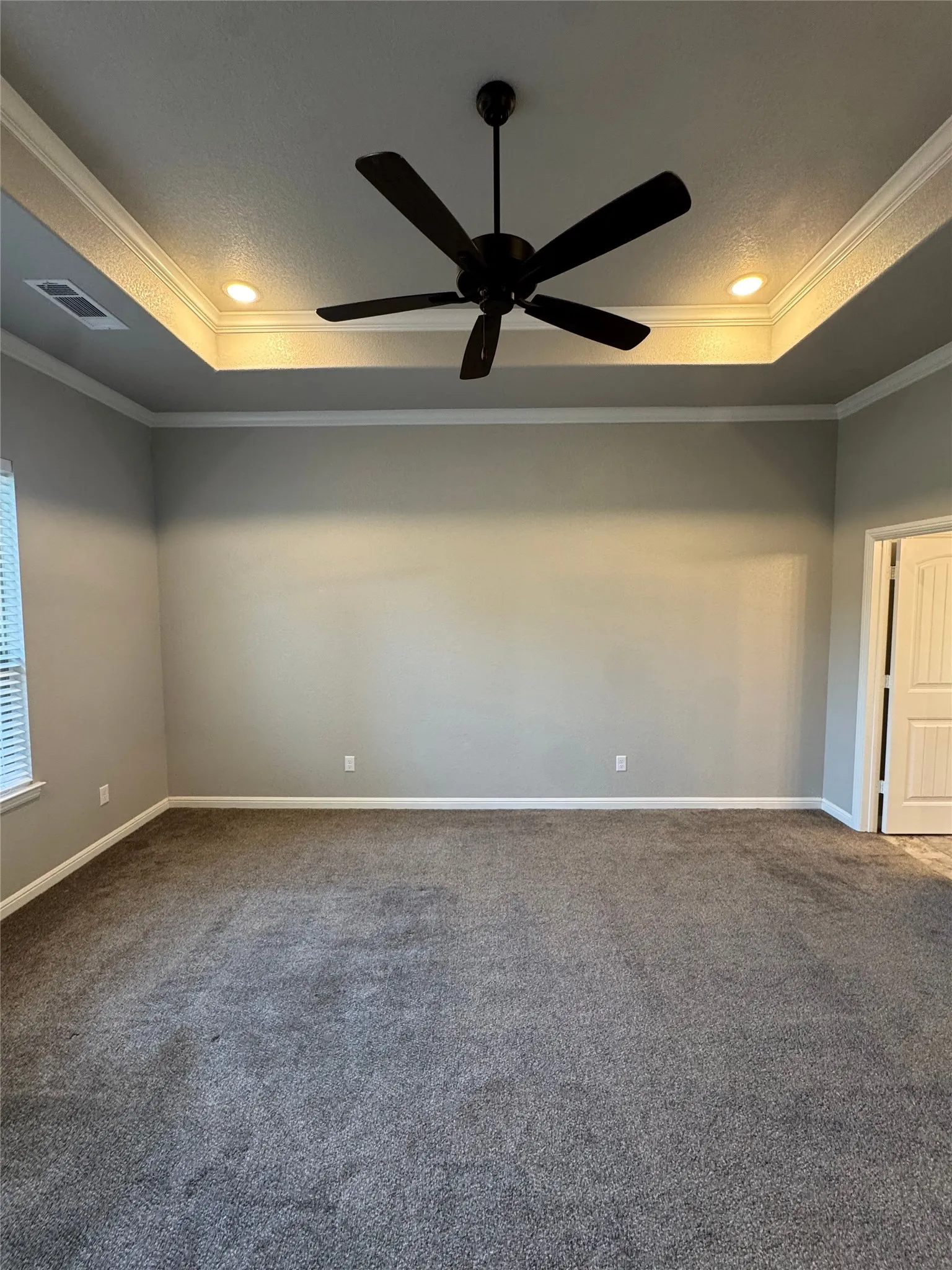 Spacious room featuring gray carpet, a tray ceiling with recessed lighting, crown molding, and a ceiling fan