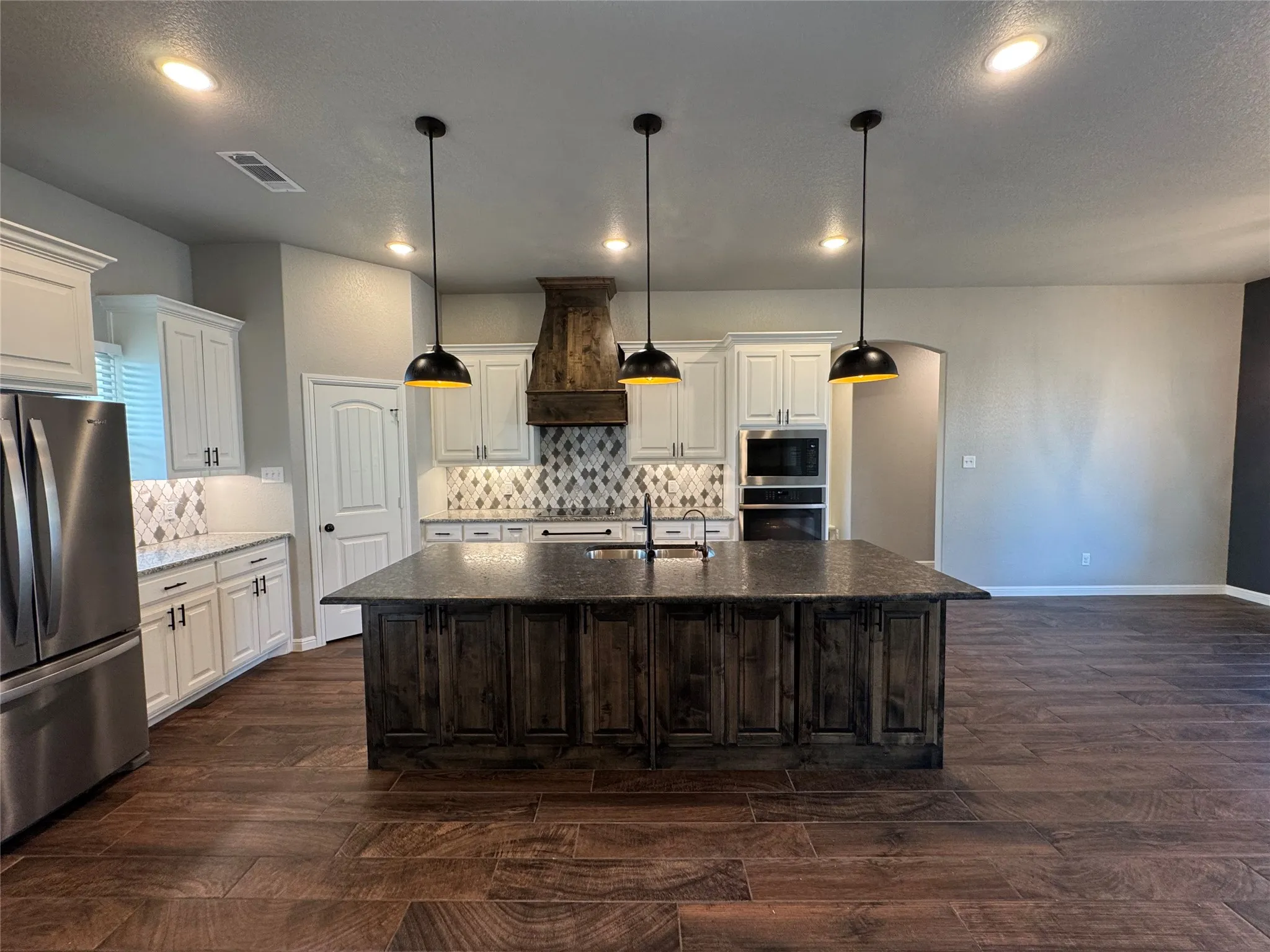 Spacious kitchen featuring an expansive center island, wood-finish flooring, white cabinetry, integrated stainless steel appliances, and a decorative range hood