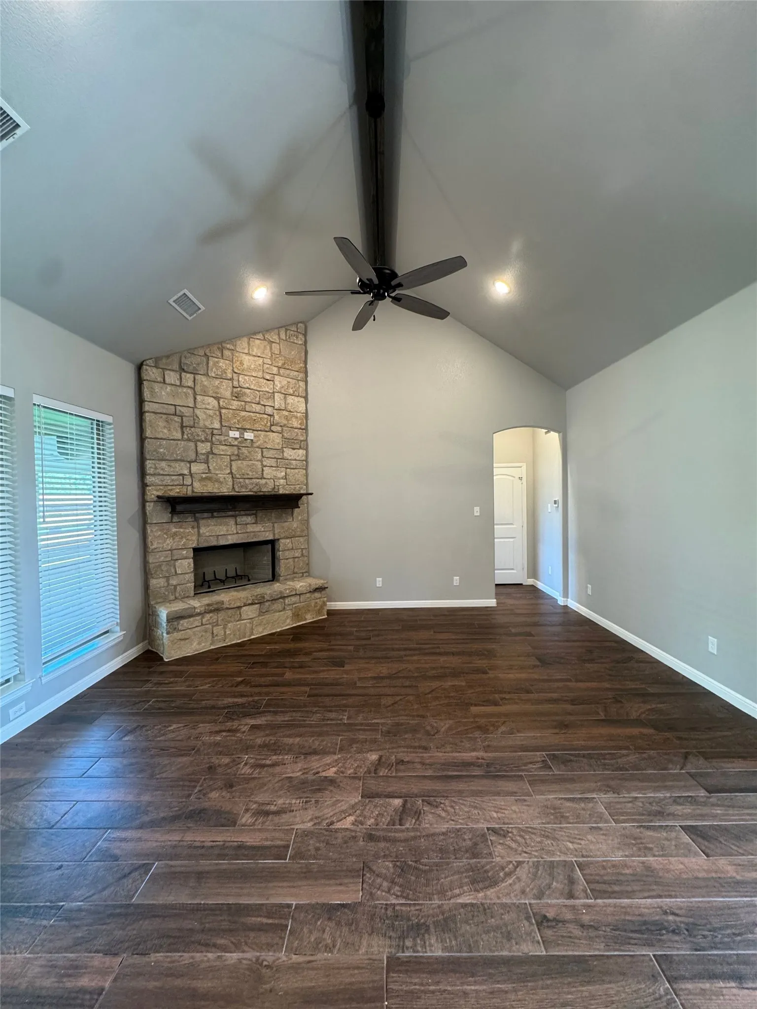 Vaulted ceiling with an exposed beam, stone-wrapped fireplace, wood-finish flooring, and recessed lighting
