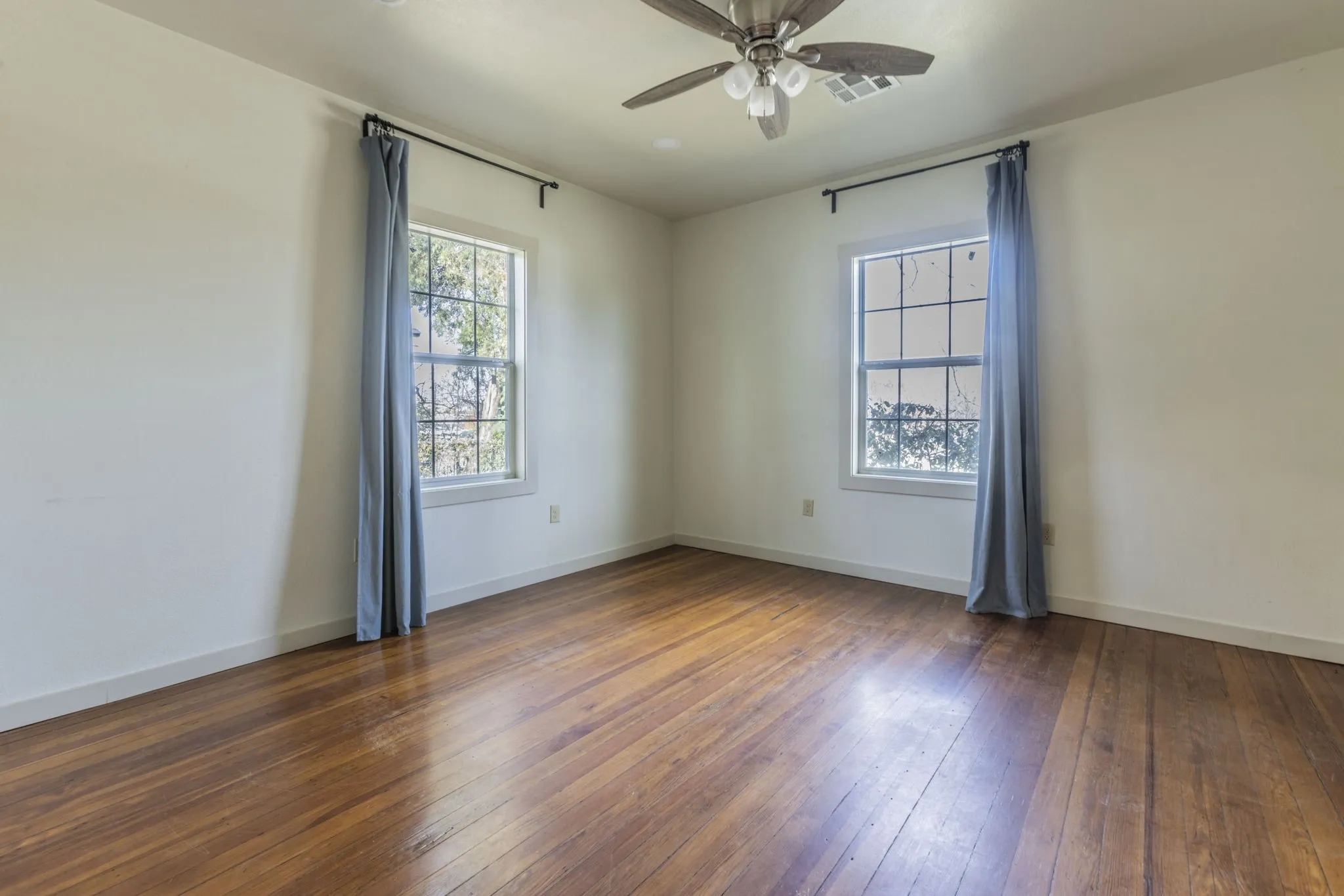 Room featuring wood-finish flooring, two large windows with white trim, and a ceiling fan with integrated lighting