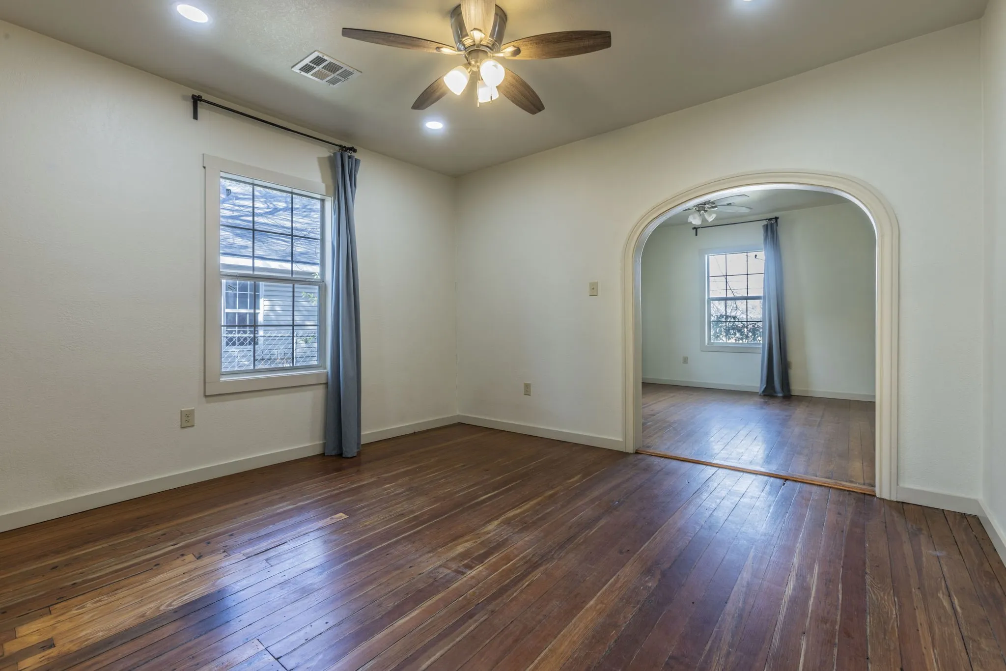 Spacious interior featuring wood-finish flooring, an arched doorway, a ceiling fan, recessed lighting, and a window with natural light