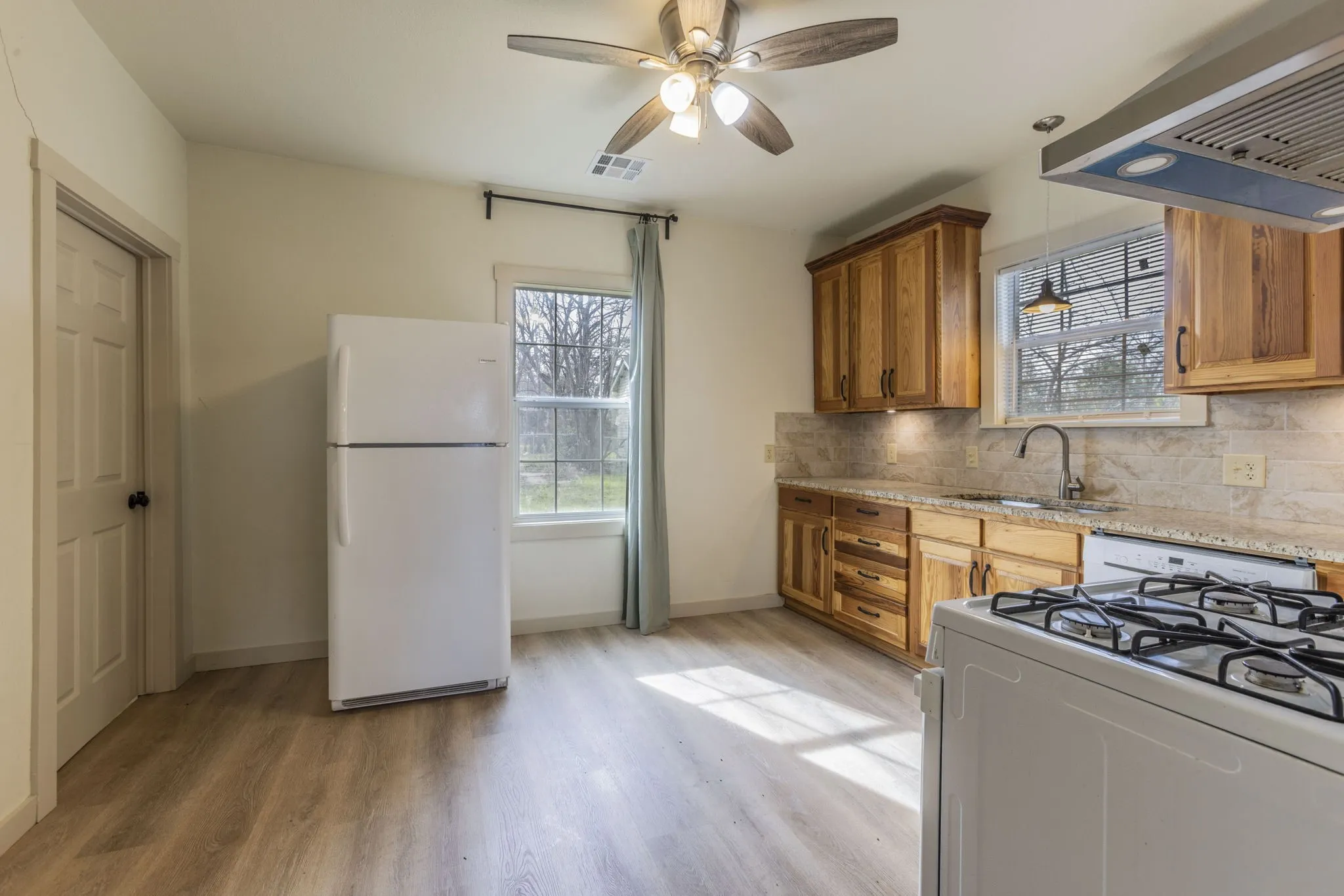 Kitchen featuring wood-finish flooring, wood cabinetry, granite-style countertops, and a tile backsplash