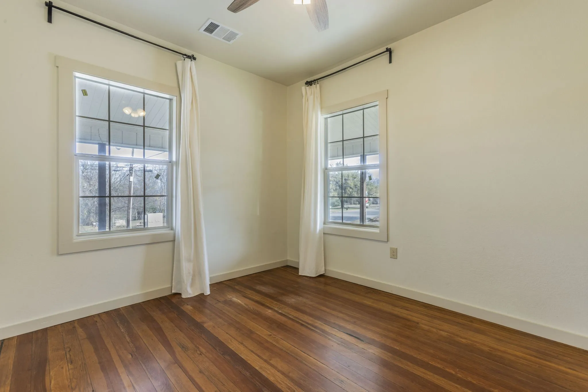 Expansive room with wood-finish flooring, two large windows with grid patterns, and a ceiling fan