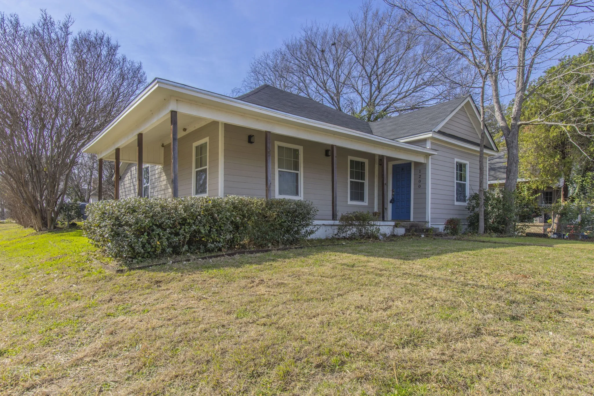 Ranch-style residence featuring a covered front porch with dark wood-finish columns, light gray siding, and a contrasting blue entry door