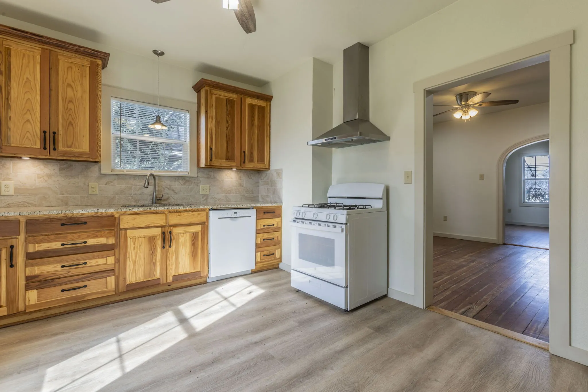 Kitchen featuring wood-finish cabinetry, light-toned countertops, a stainless steel range hood, a white gas range, and a white dishwasher