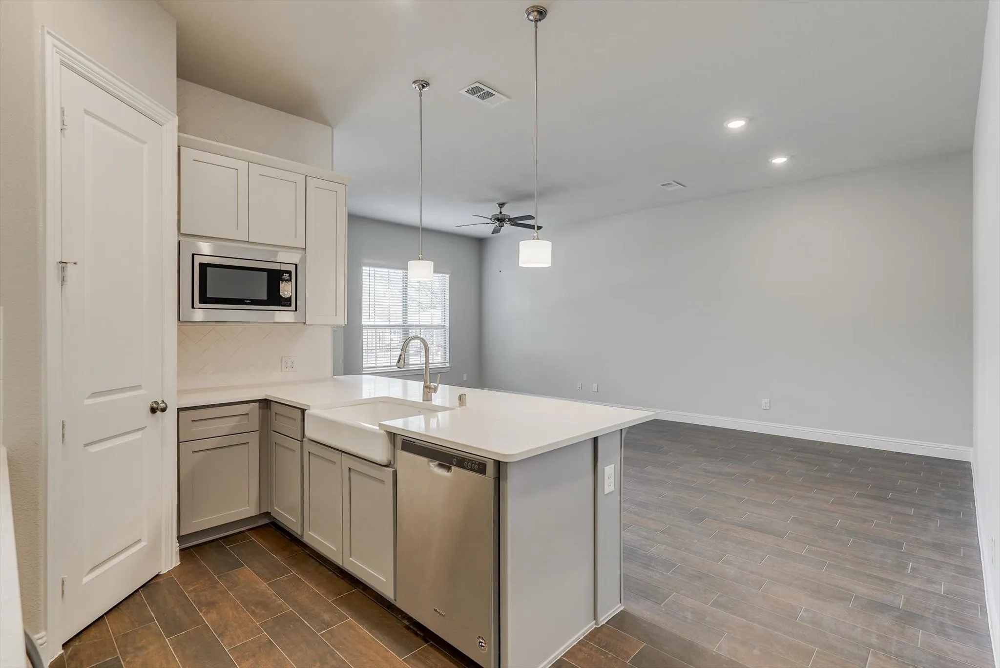 Kitchen island with pendant lighting, stainless steel appliances, light-toned cabinetry, wood-finish flooring, and recessed lighting