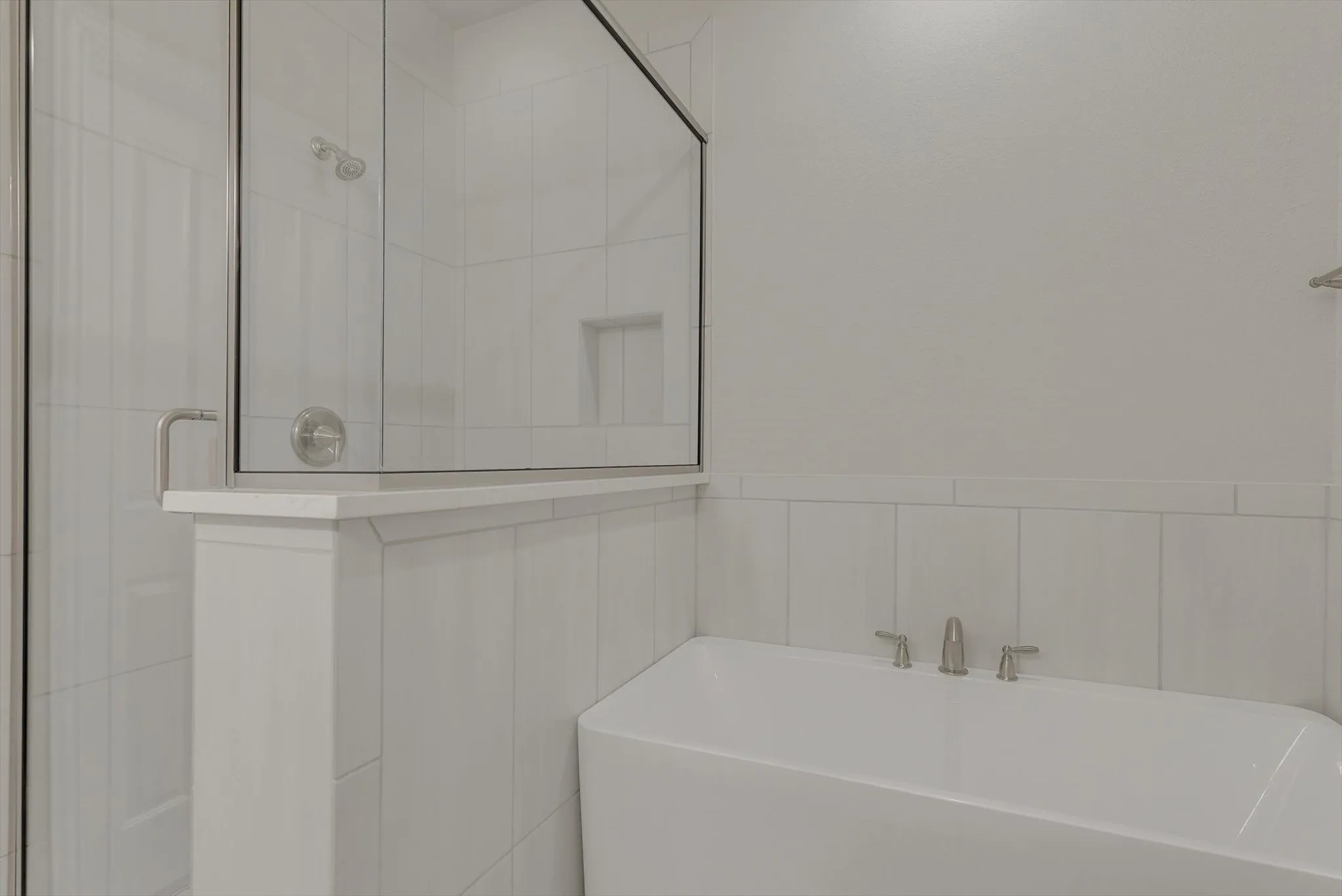 White tiled shower with a glass enclosure, an integrated shower niche, and a separate soaking tub with brushed nickel fixtures