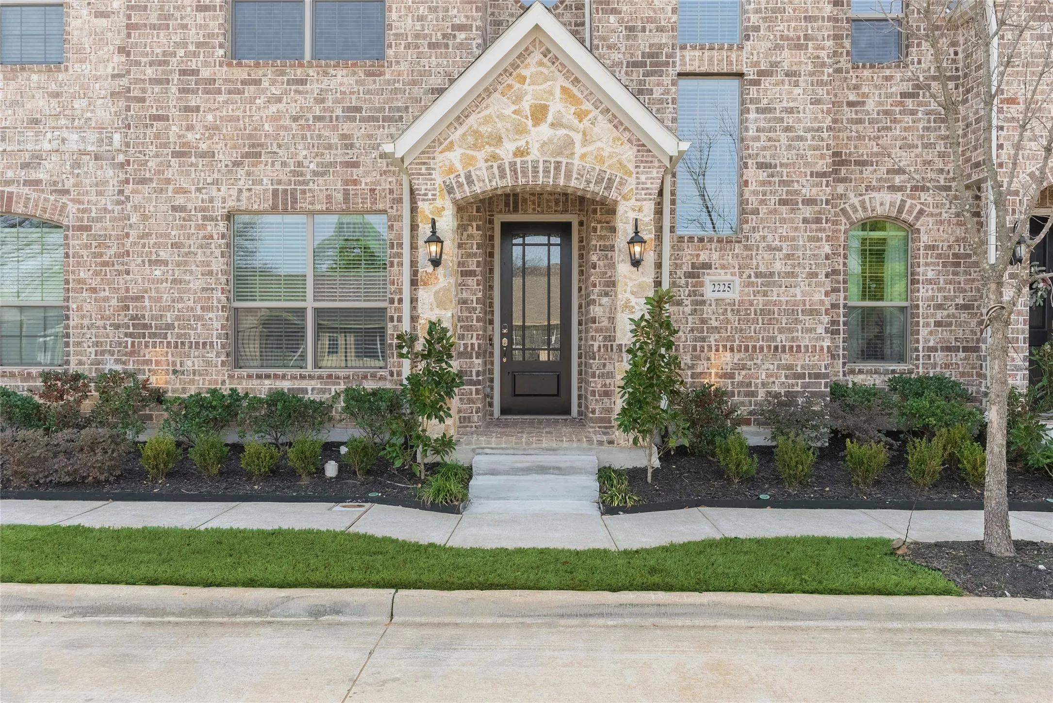 Brick facade with stone accents, covered entryway, and two exterior sconce lights