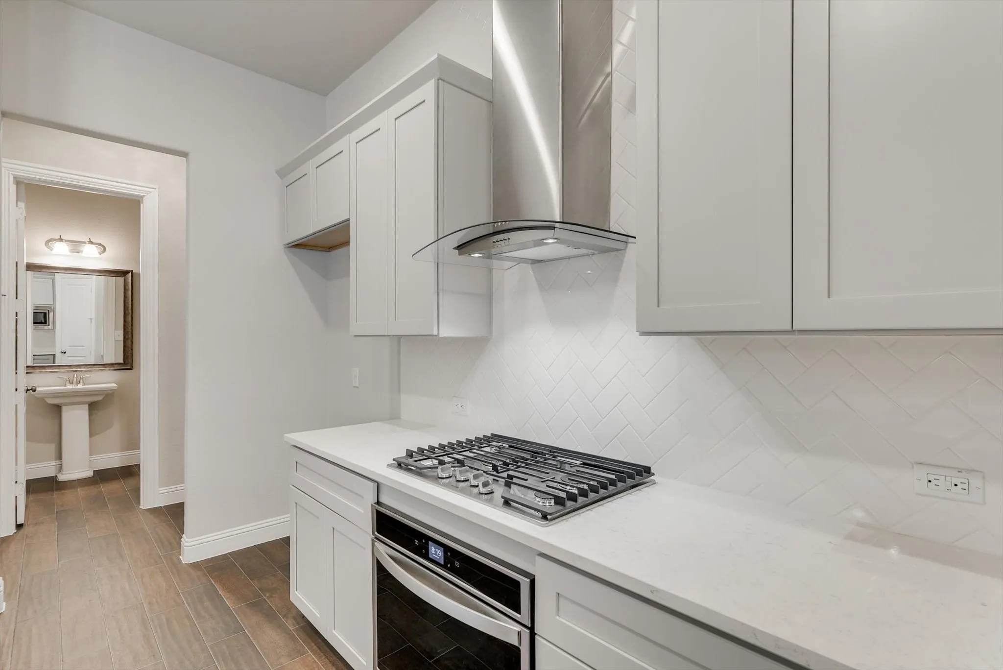 White shaker-style cabinetry, stainless steel range hood, built-in gas cooktop, quartz countertops, and a white herringbone tile backsplash