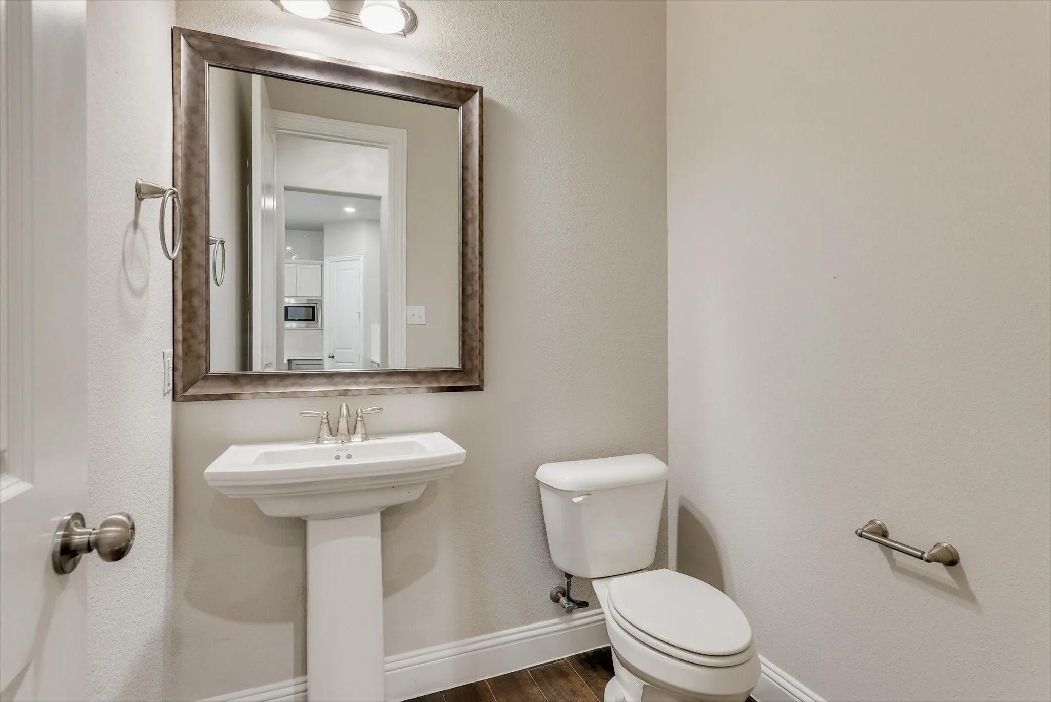 Pedestal sink with chrome-finish faucet, framed wall mirror, and overhead vanity lighting