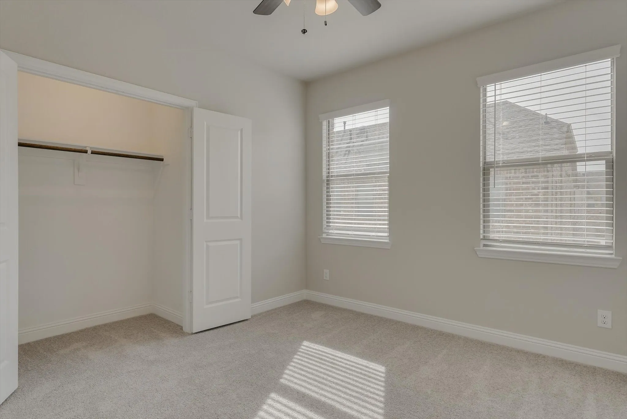 Carpeted room featuring two windows with blinds, a ceiling fan, and a built-in closet with bi-fold doors