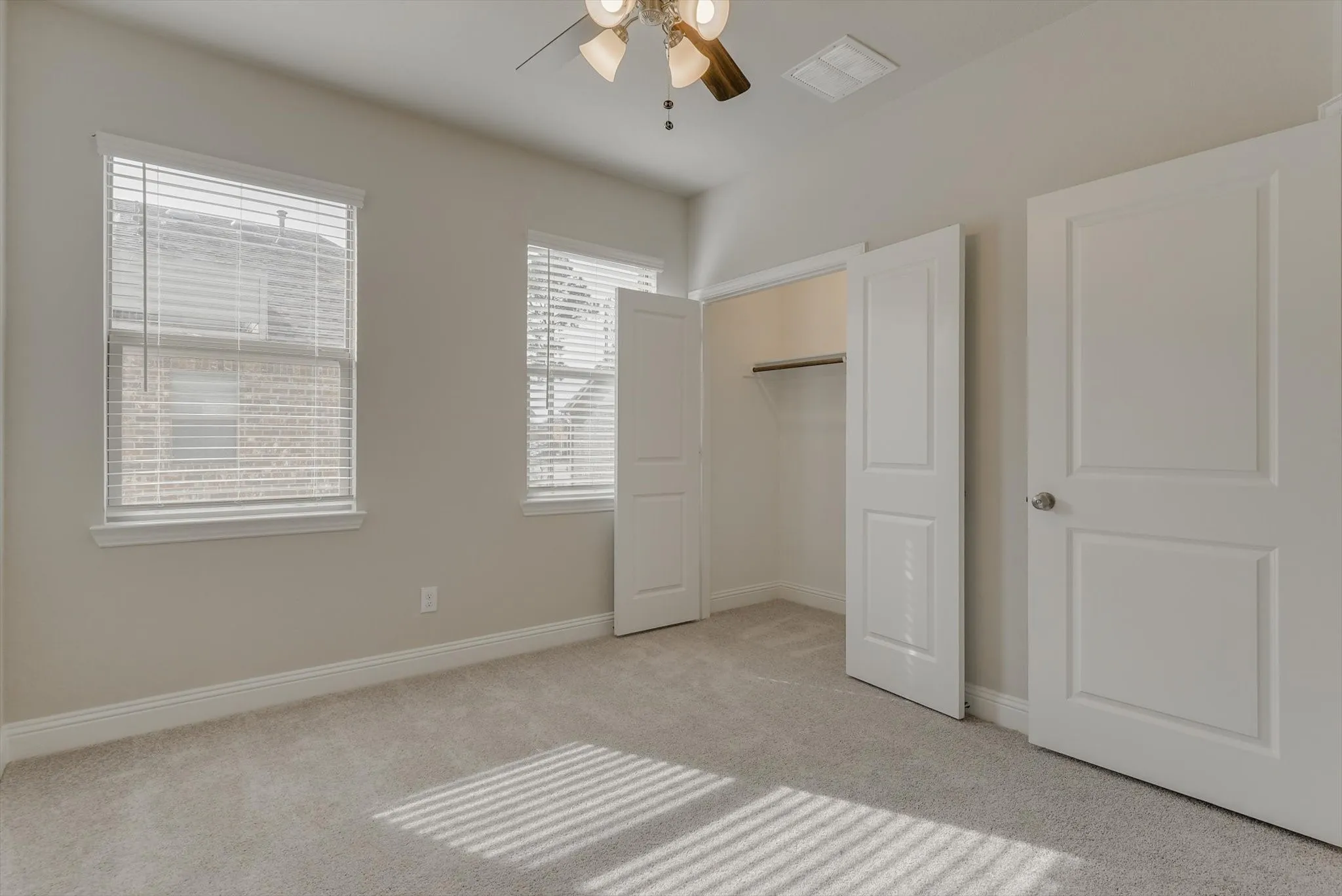 Neutral wall paint with carpet flooring, two windows with blinds, a ceiling fan with light fixture, and a built-in closet with a hanging rod