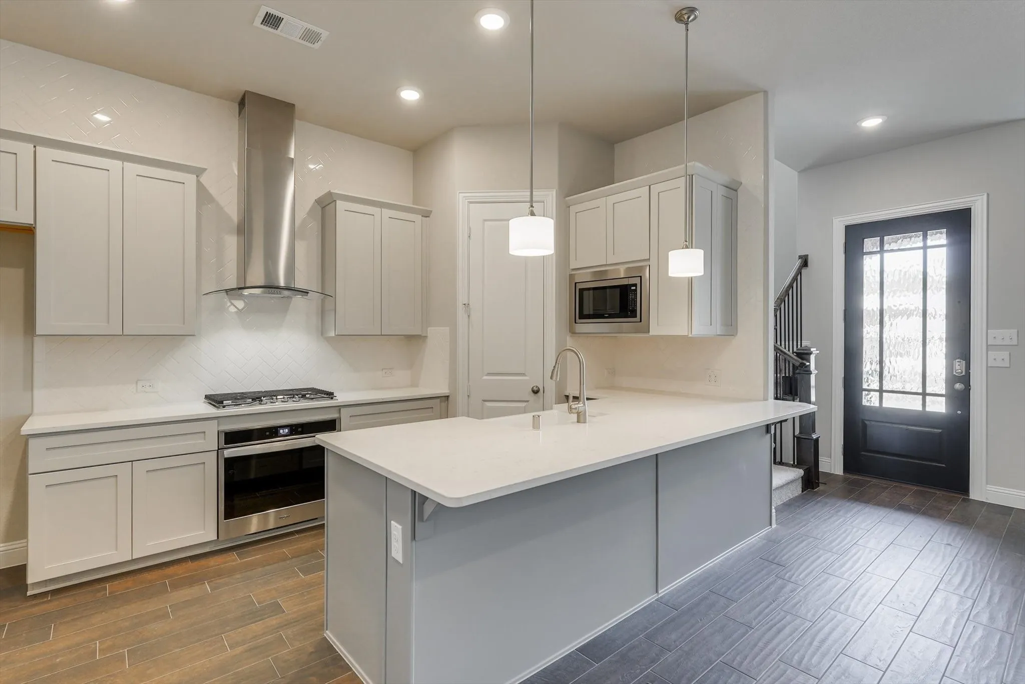 Kitchen with light gray cabinetry, stainless steel appliances, a white tile backsplash, and a central island with a sink and pendant lighting