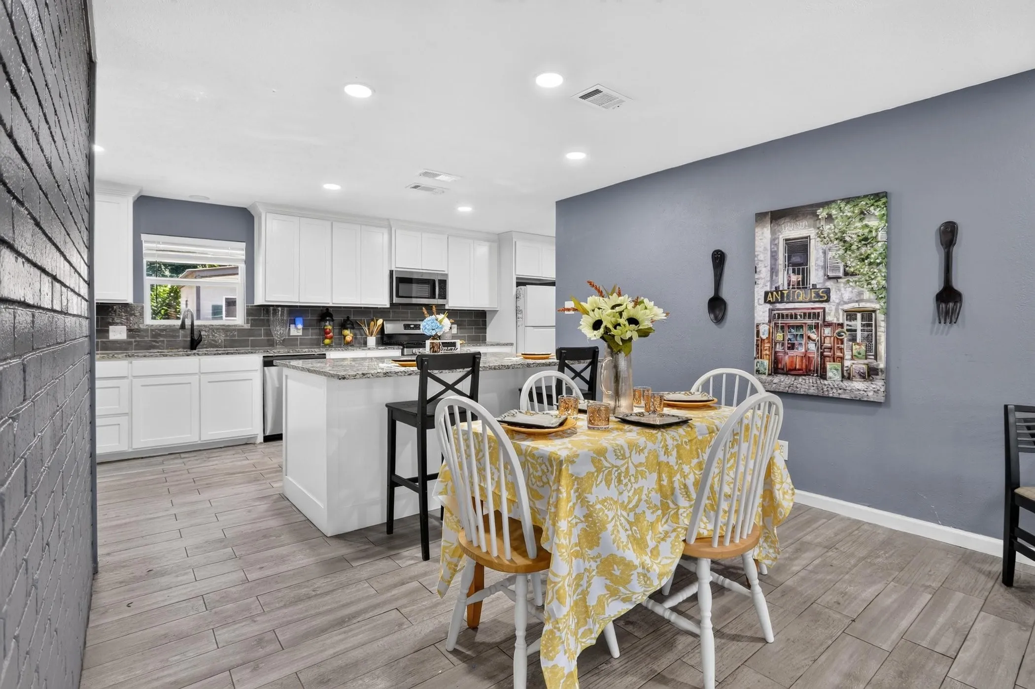 Open-concept kitchen and dining area featuring white cabinetry with stainless steel appliances, wood-finish flooring throughout, and a center island with seating
