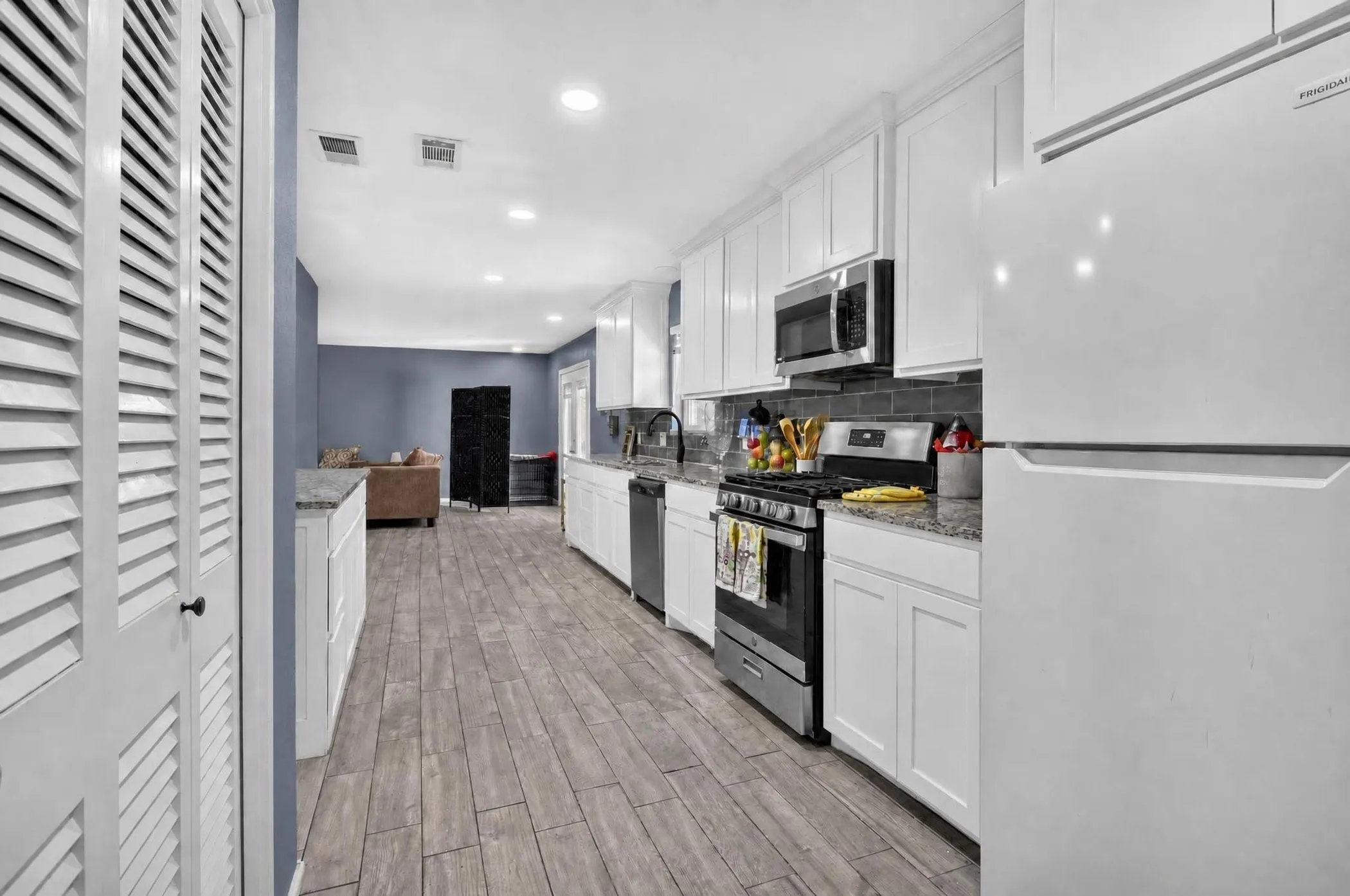 Modern kitchen featuring white cabinetry, stainless steel appliances including a gas range and built-in microwave, quartz countertops, and wood-finish flooring that extends into the adjoining living areas