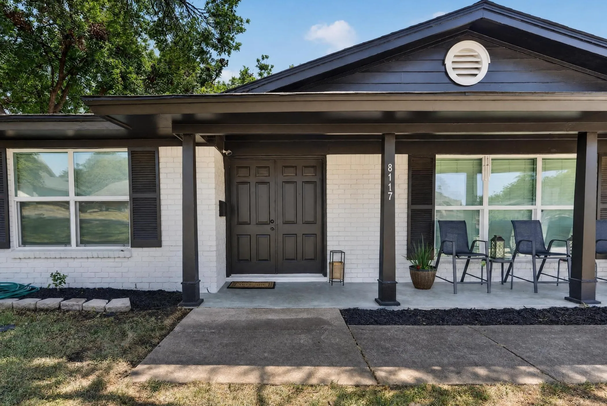 White brick exterior with dark trim and shutters, covered front porch, and double entry doors