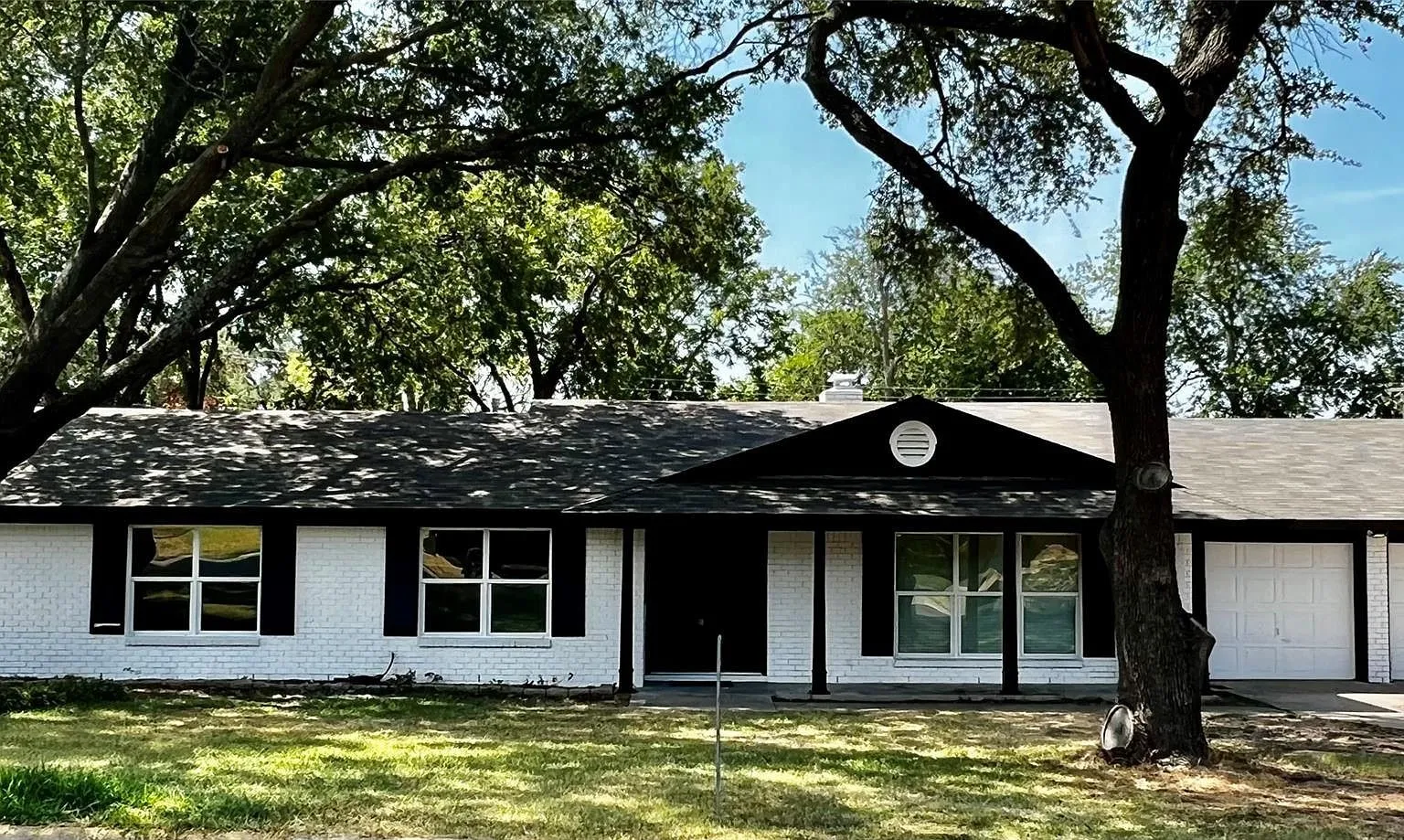 White painted brick exterior with black shutters, multiple front-facing windows, and an attached two-car garage