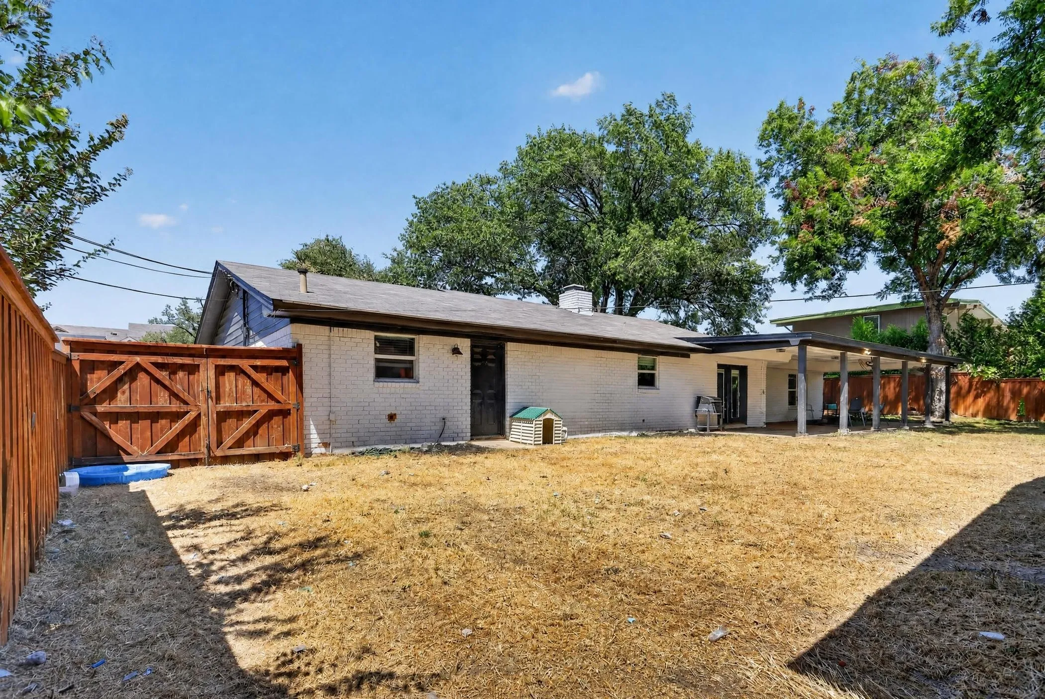 Spacious residential property featuring a brick exterior, covered porch with wooden support beams, and a large cleared lot with mature trees