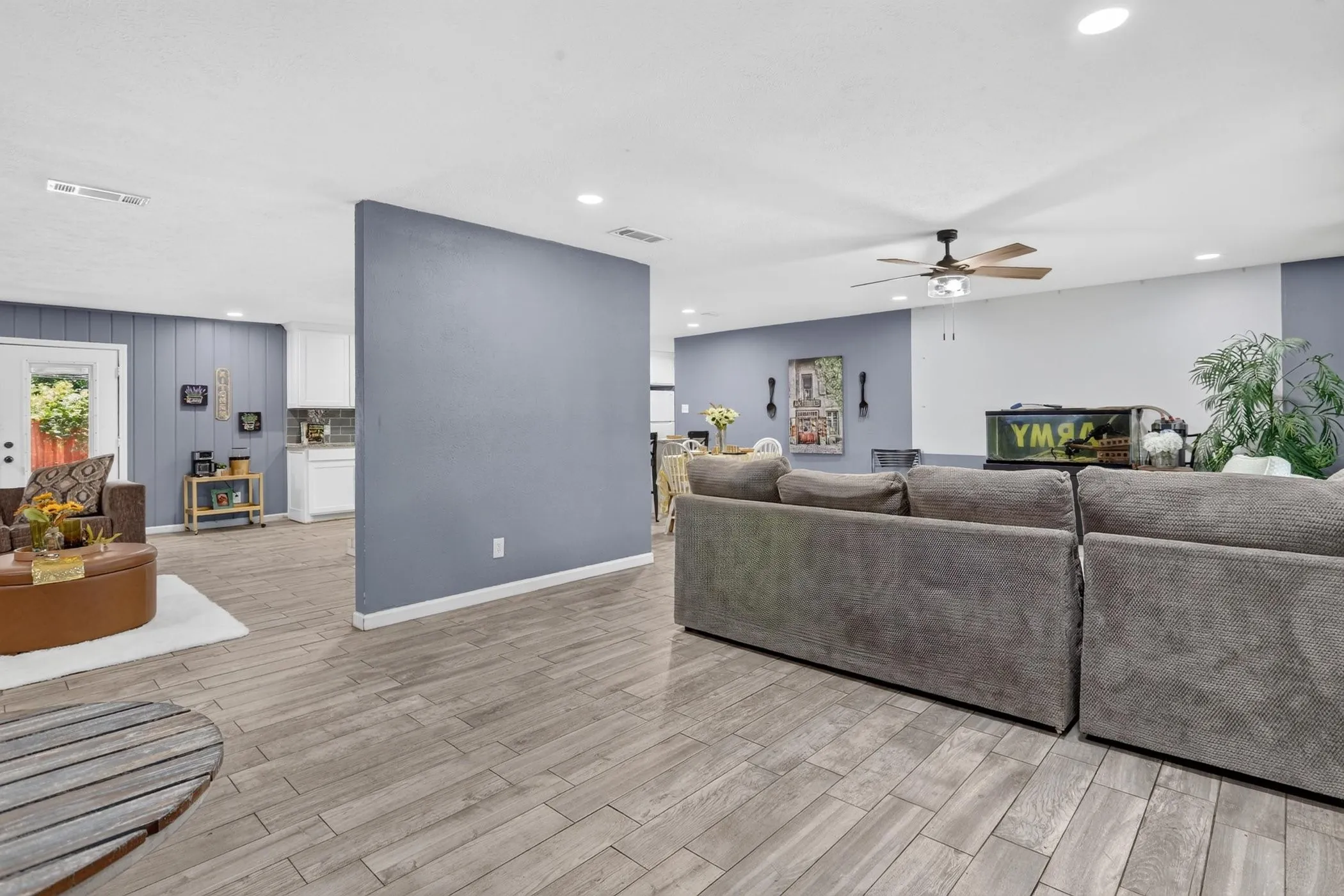 Open-concept living area featuring plank-style wood-finish flooring, a large architectural accent wall in slate blue, recessed ceiling lighting, and a ceiling fan