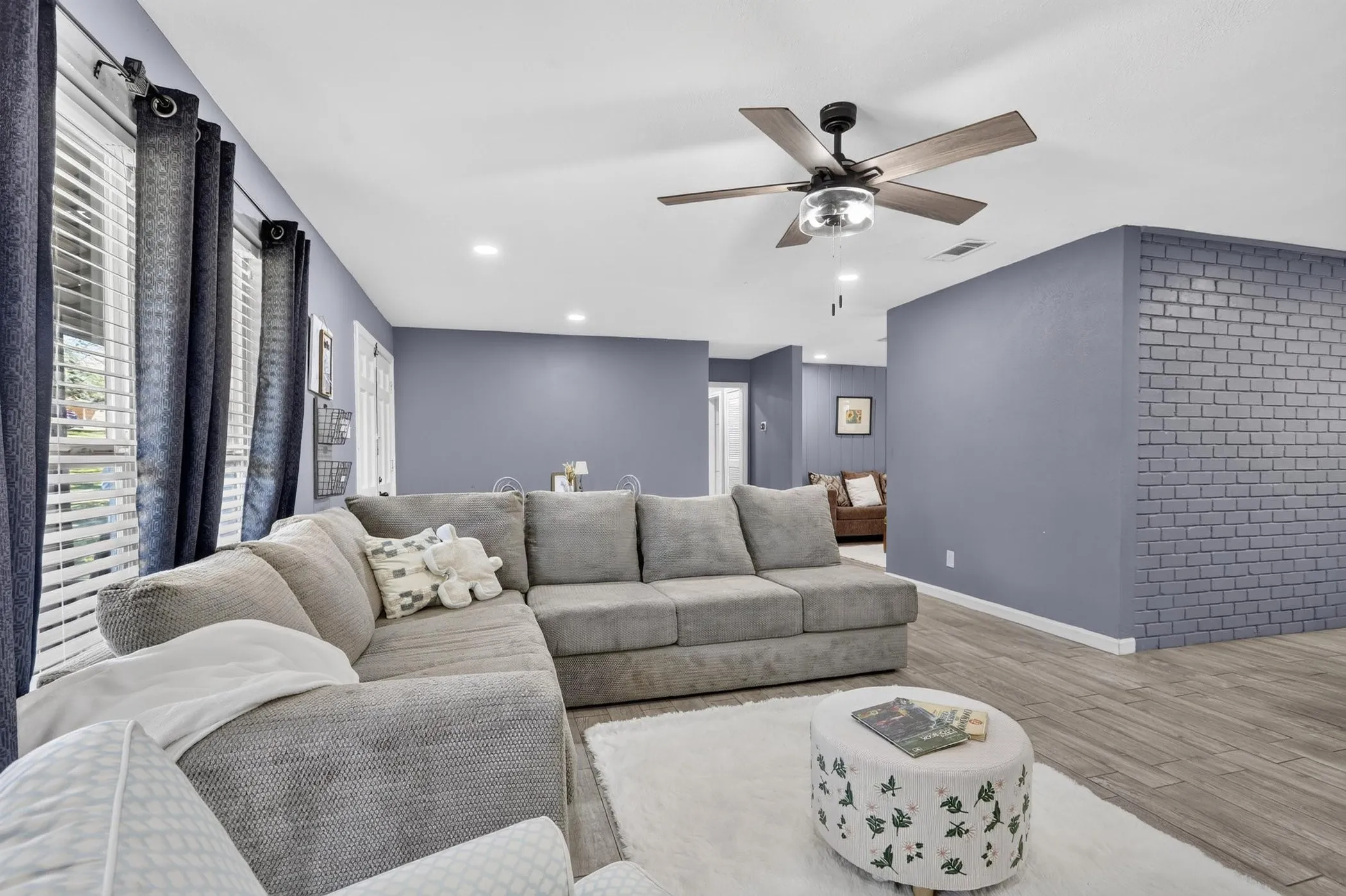 Spacious living room featuring a sectional layout with neutral upholstery, wood-finish flooring throughout, and recessed ceiling lighting