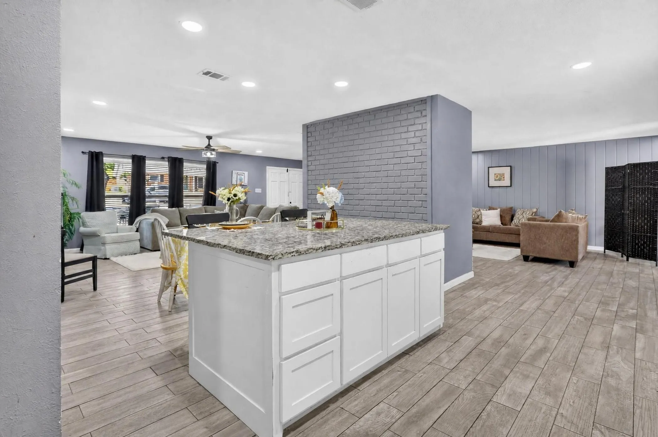 Open-concept kitchen and living area featuring a white cabinetry island with wood-finish countertops, stainless steel appliances, gray subway tile backsplash, recessed ceiling lighting, and wood-finish flooring throughout