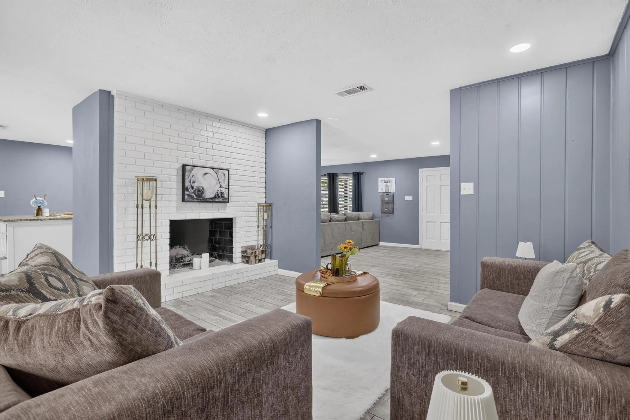 Spacious primary living area featuring a white subway brick fireplace with hearth, light wood-finish flooring, and recessed ceiling lighting
