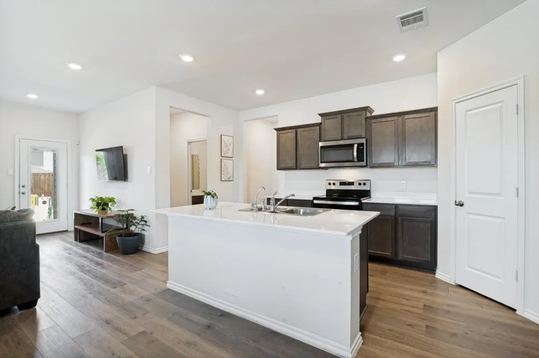 Kitchen with wood-finish flooring, dark wood-finish cabinetry, stainless steel appliances, and a central island with a white quartz countertop