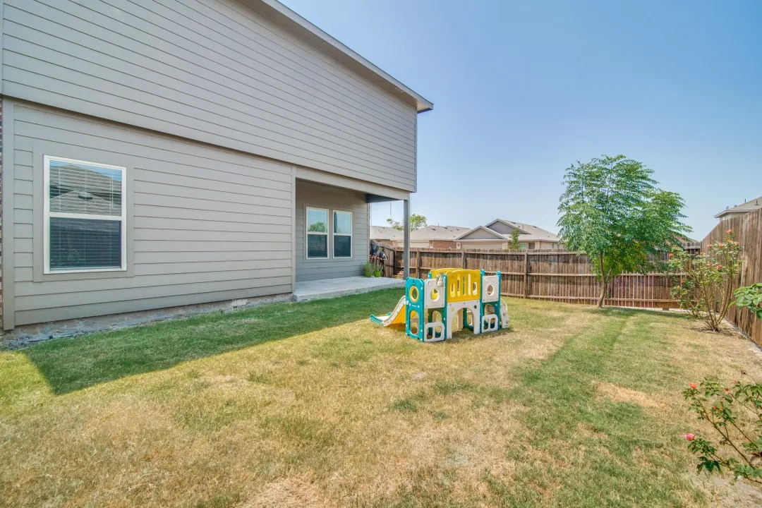 Expansive backyard featuring a wood-panel fence, mature trees, and a concrete patio