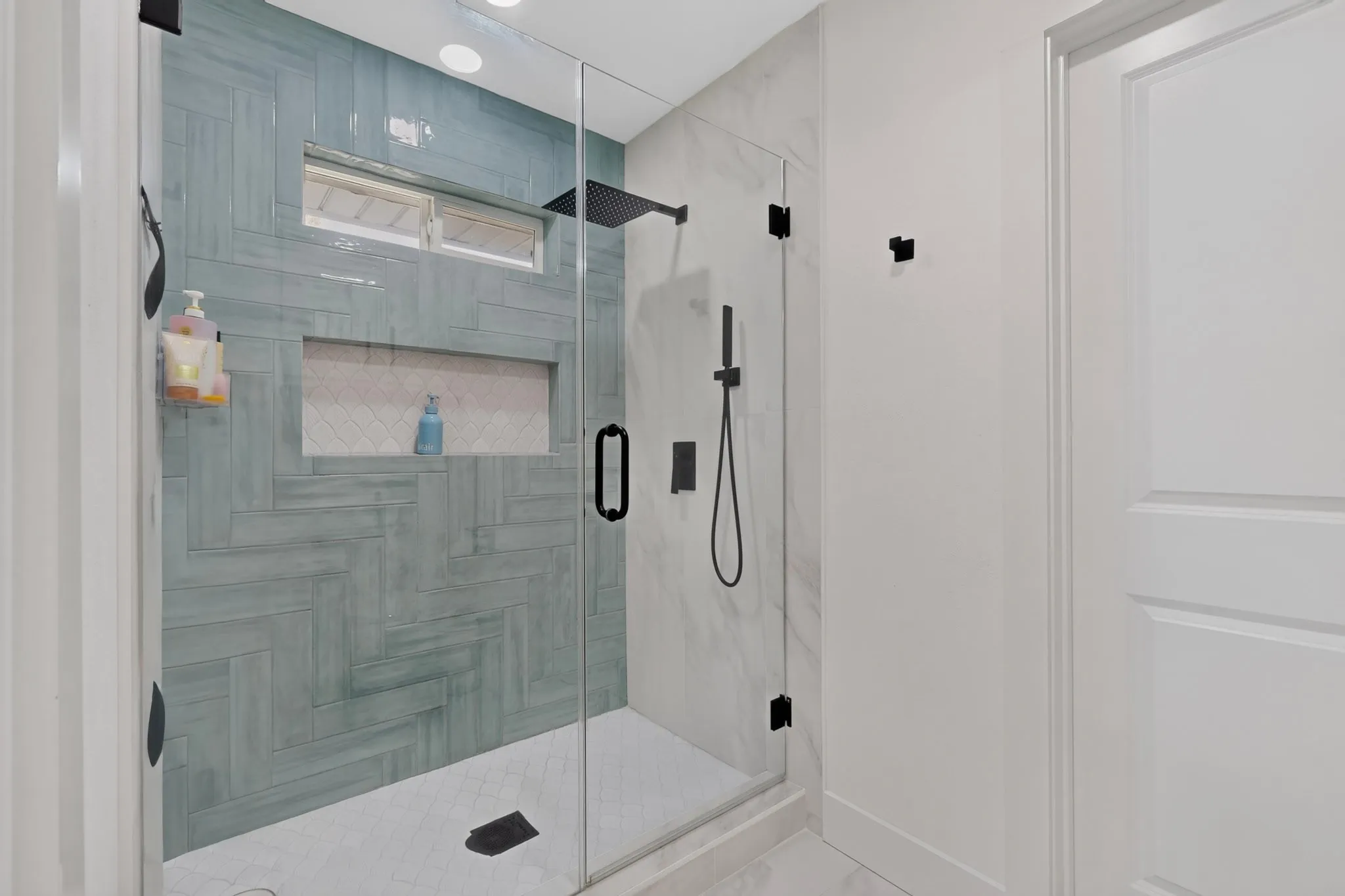 Glass-enclosed shower with a herringbone-patterned accent wall, recessed shower niche, and matte black fixtures