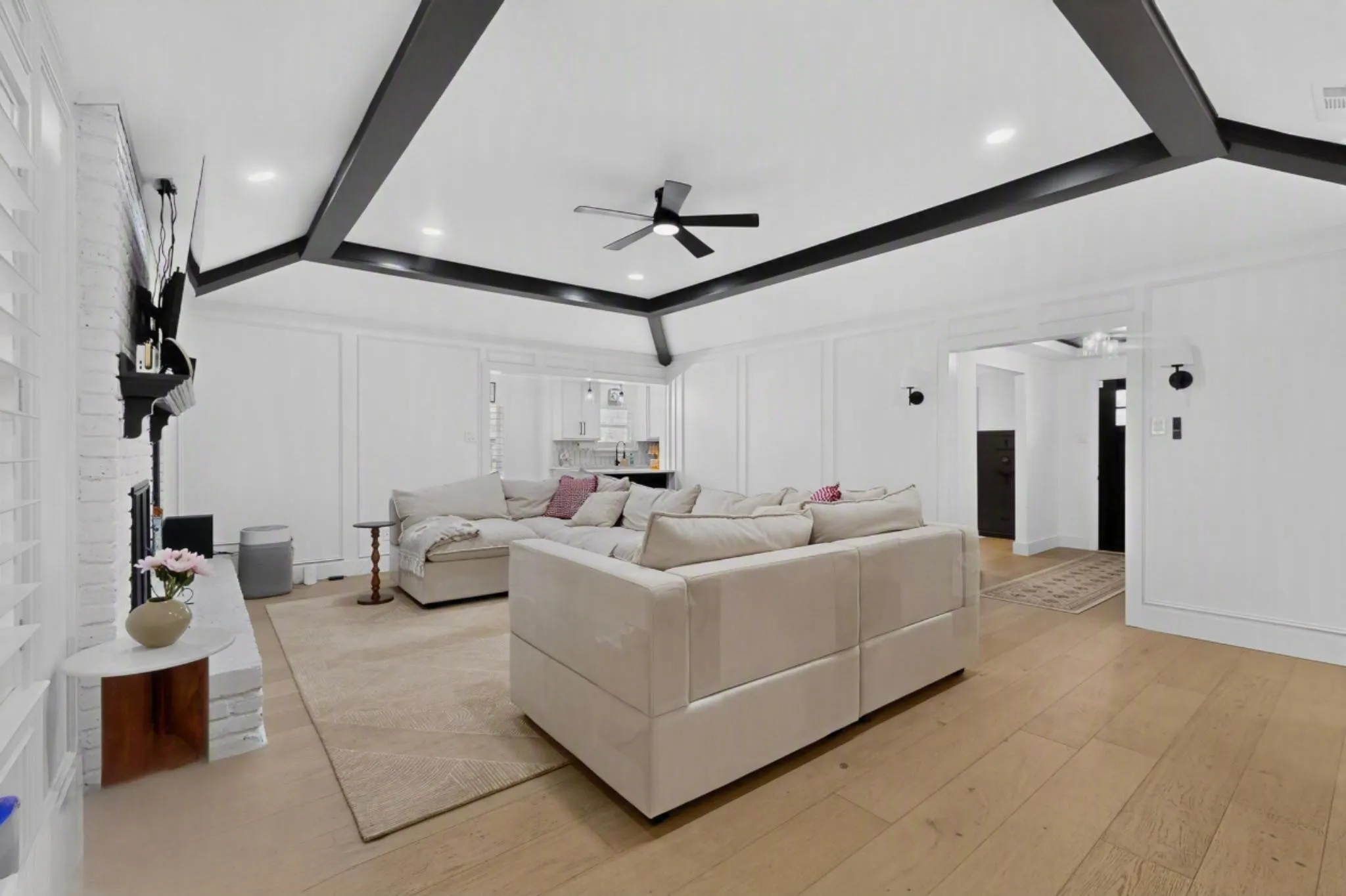 Vaulted ceiling with exposed beams, recessed lighting, wood-finish flooring, white brick fireplace, and wall paneling