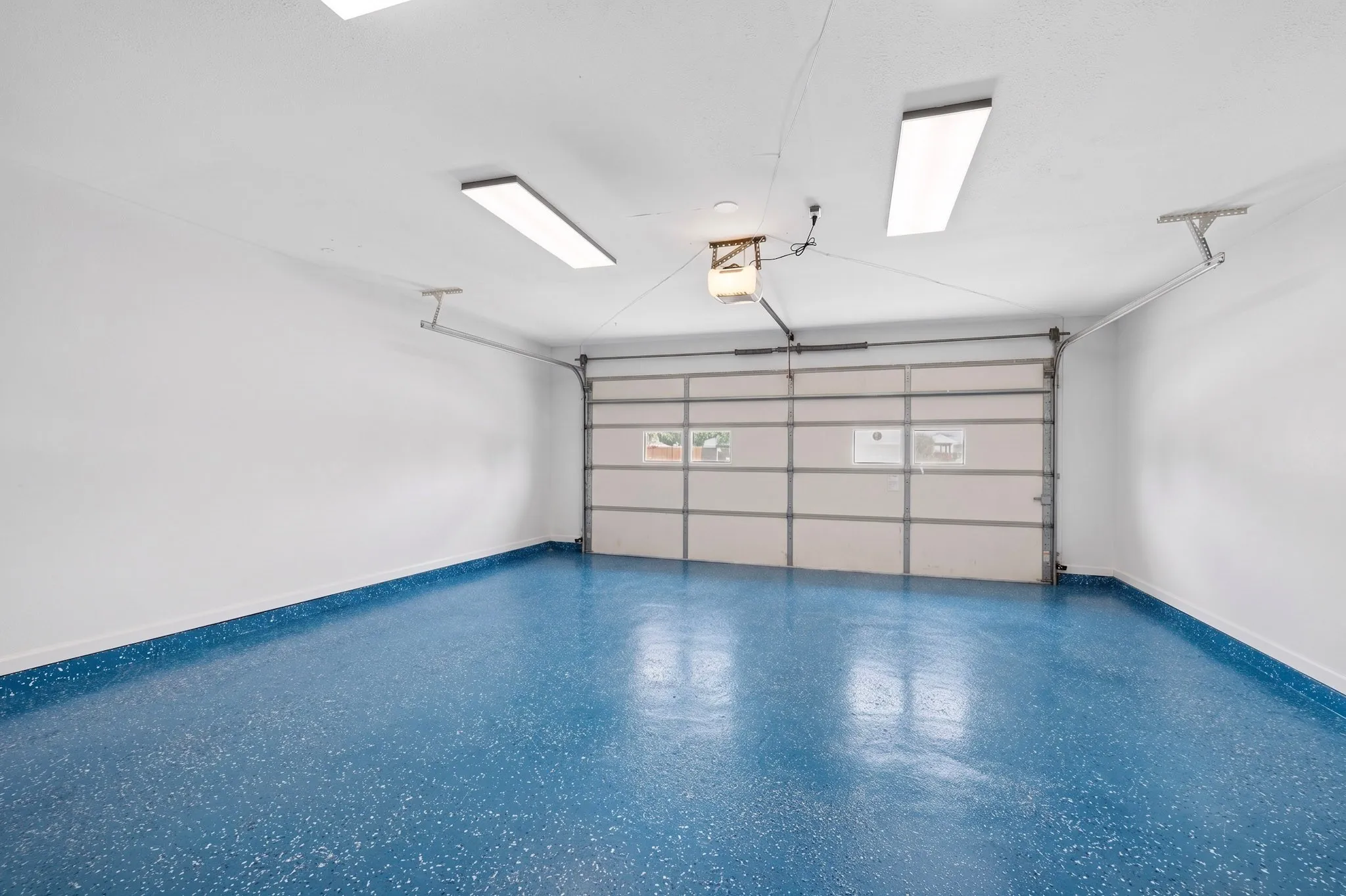 Interior garage with a glossy blue speckled epoxy floor finish, white painted floors, and overhead fluorescent lighting fixtures
