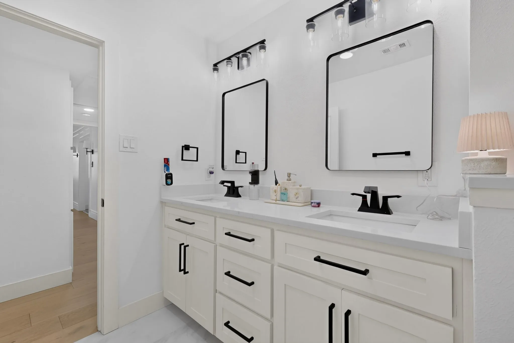 Dual vanity with integrated sinks, white cabinetry with black hardware, black framed mirrors, and black wall-mounted light fixtures