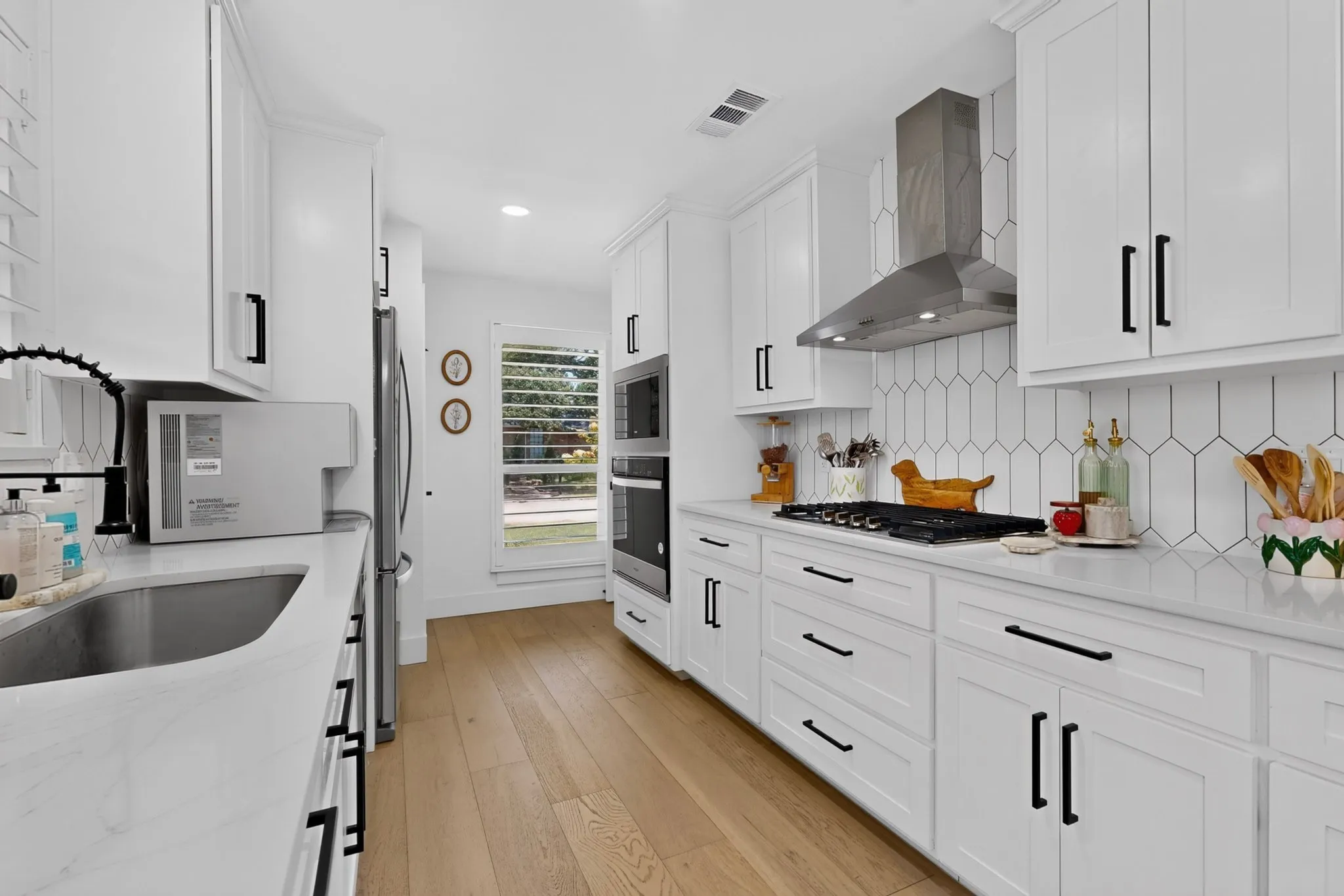 White cabinetry with black hardware, wood-finish flooring, stainless steel appliances, white countertops, and a full-height tile backsplash