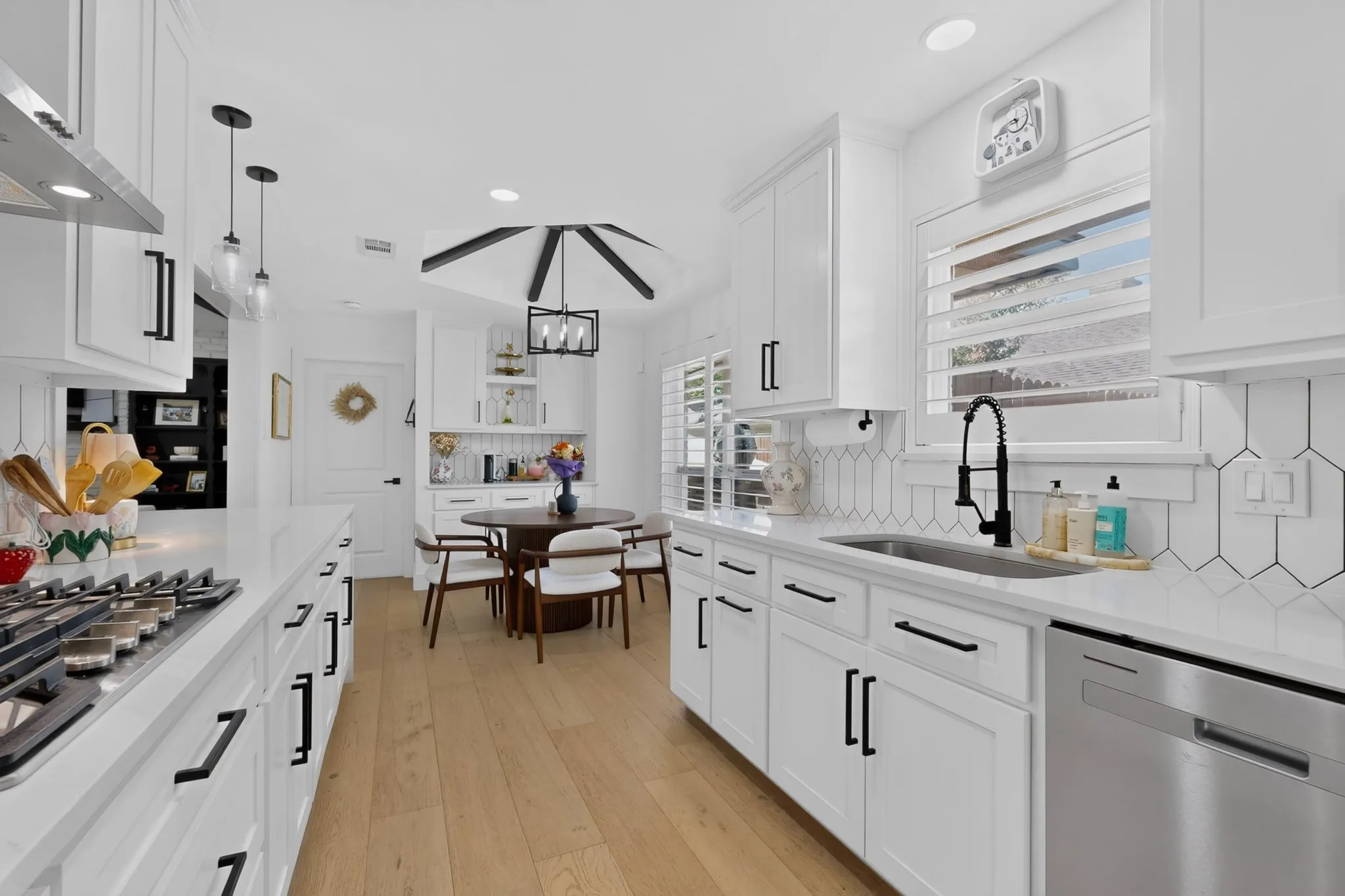 White cabinetry with black hardware, wood-finish flooring, stainless steel appliances, geometric tile backsplash, and recessed lighting