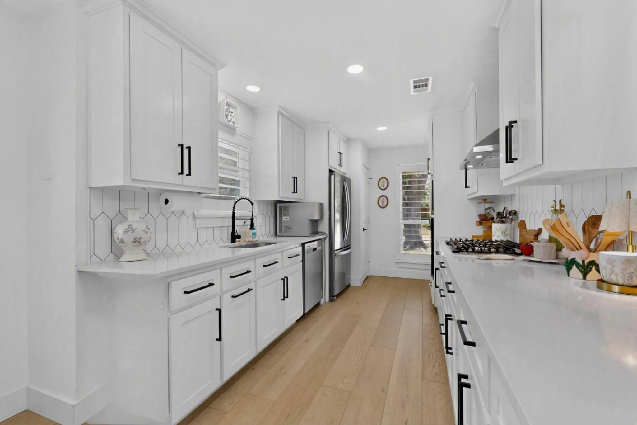White cabinetry with black hardware, wood-finish flooring, white countertops, hexagon tile backsplash, and stainless steel appliances