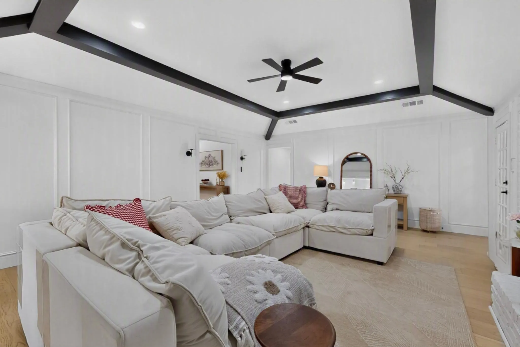 White paneled walls, light wood-finish flooring, exposed black ceiling beams, recessed lighting, and a ceiling fan