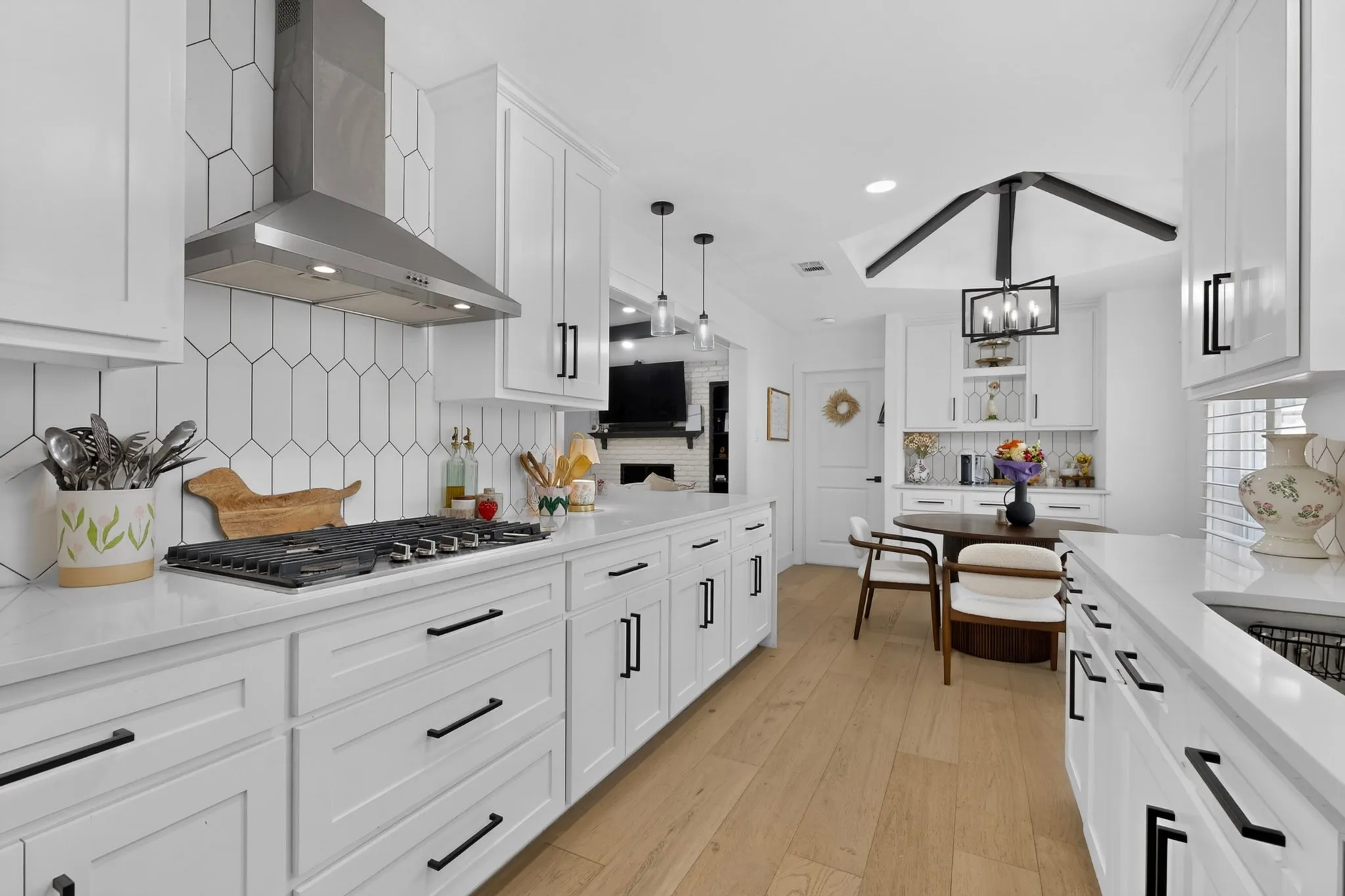 White cabinetry, integrated gas cooktop, stainless steel range hood, light wood-finish flooring, and a decorative ceiling fixture