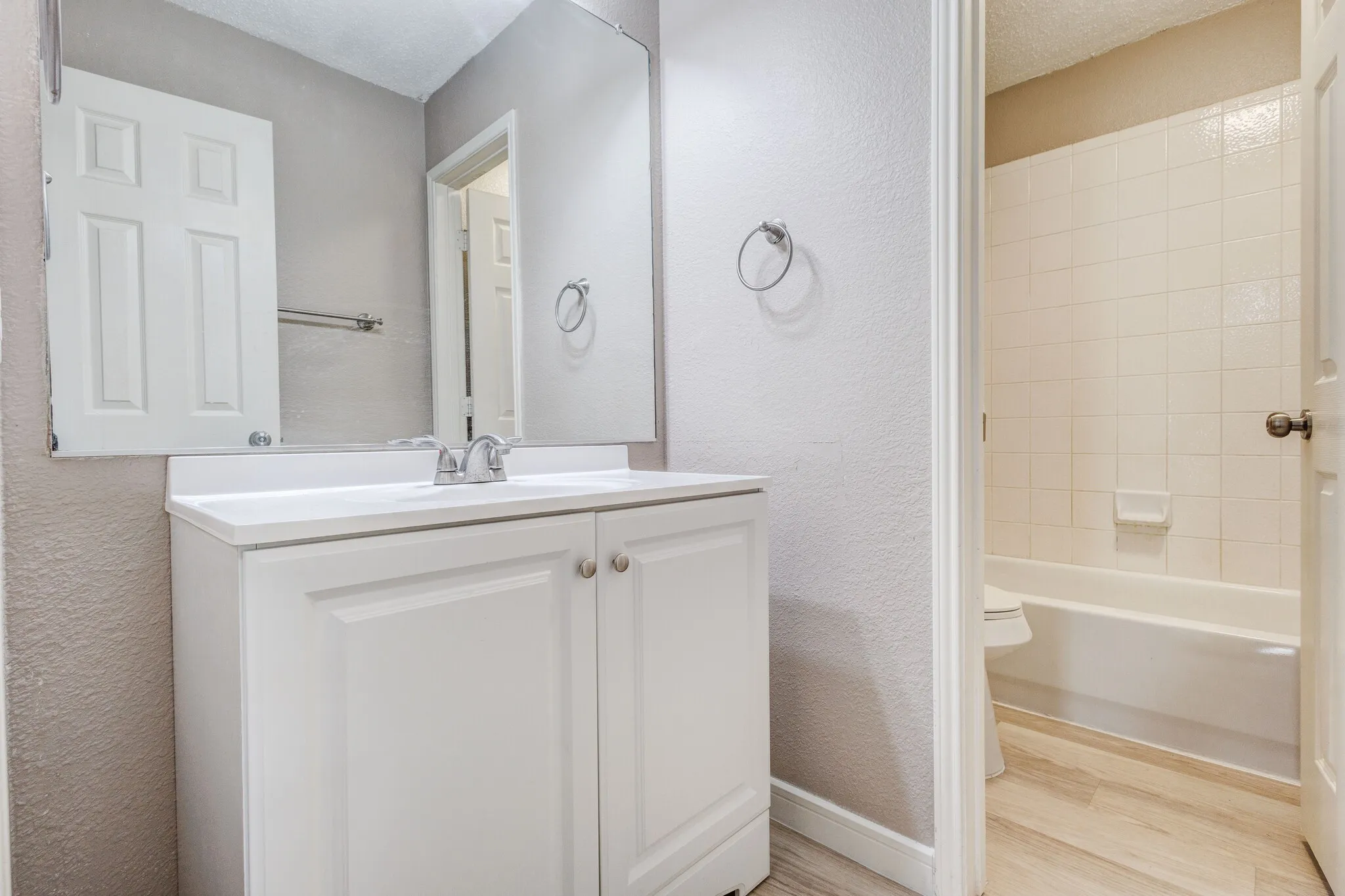 Bathroom vanity featuring a white cabinet with silver-toned hardware, an integrated sink, and a large wall-mounted mirror
