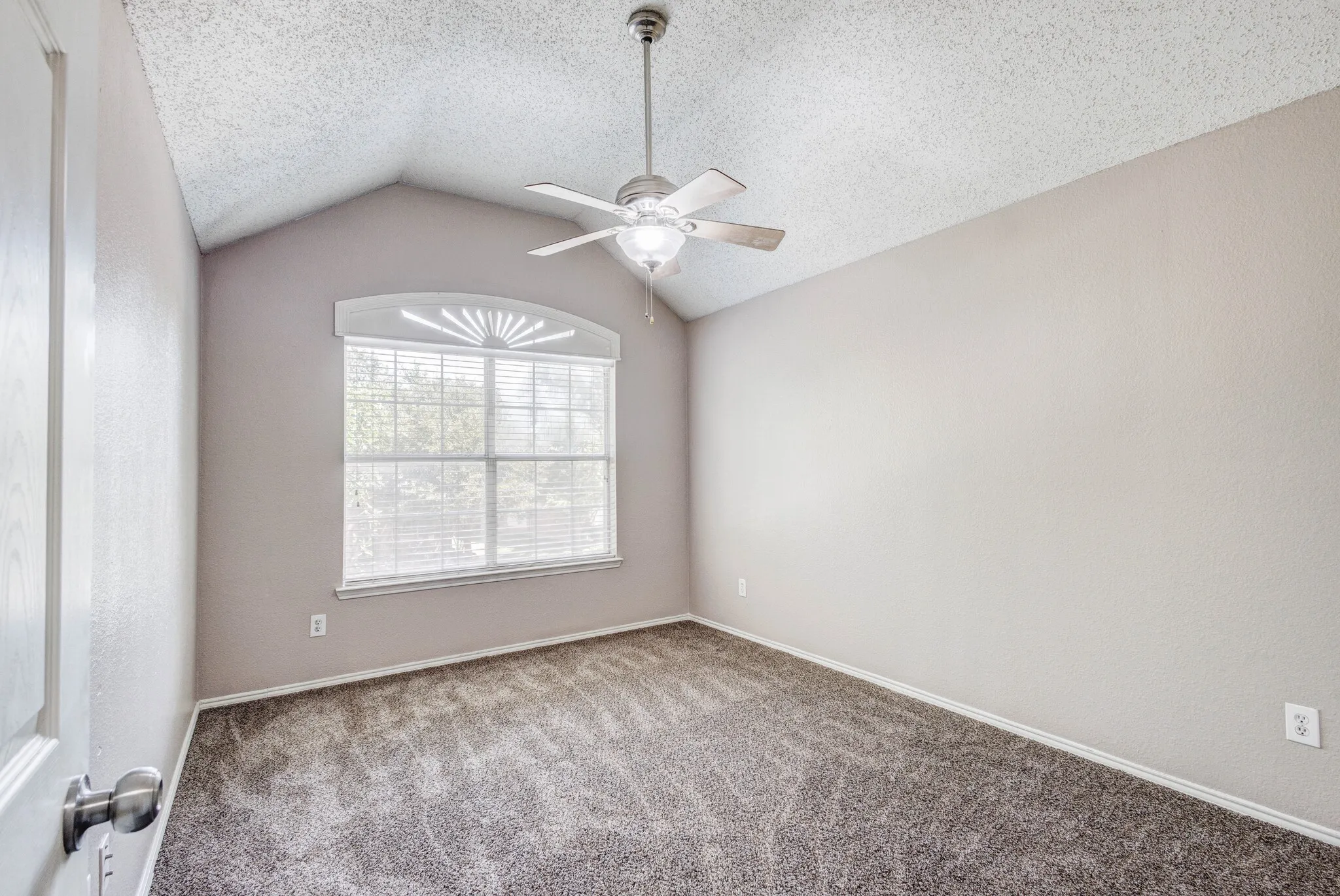Vaulted ceiling room with textured walls and plush carpet flooring