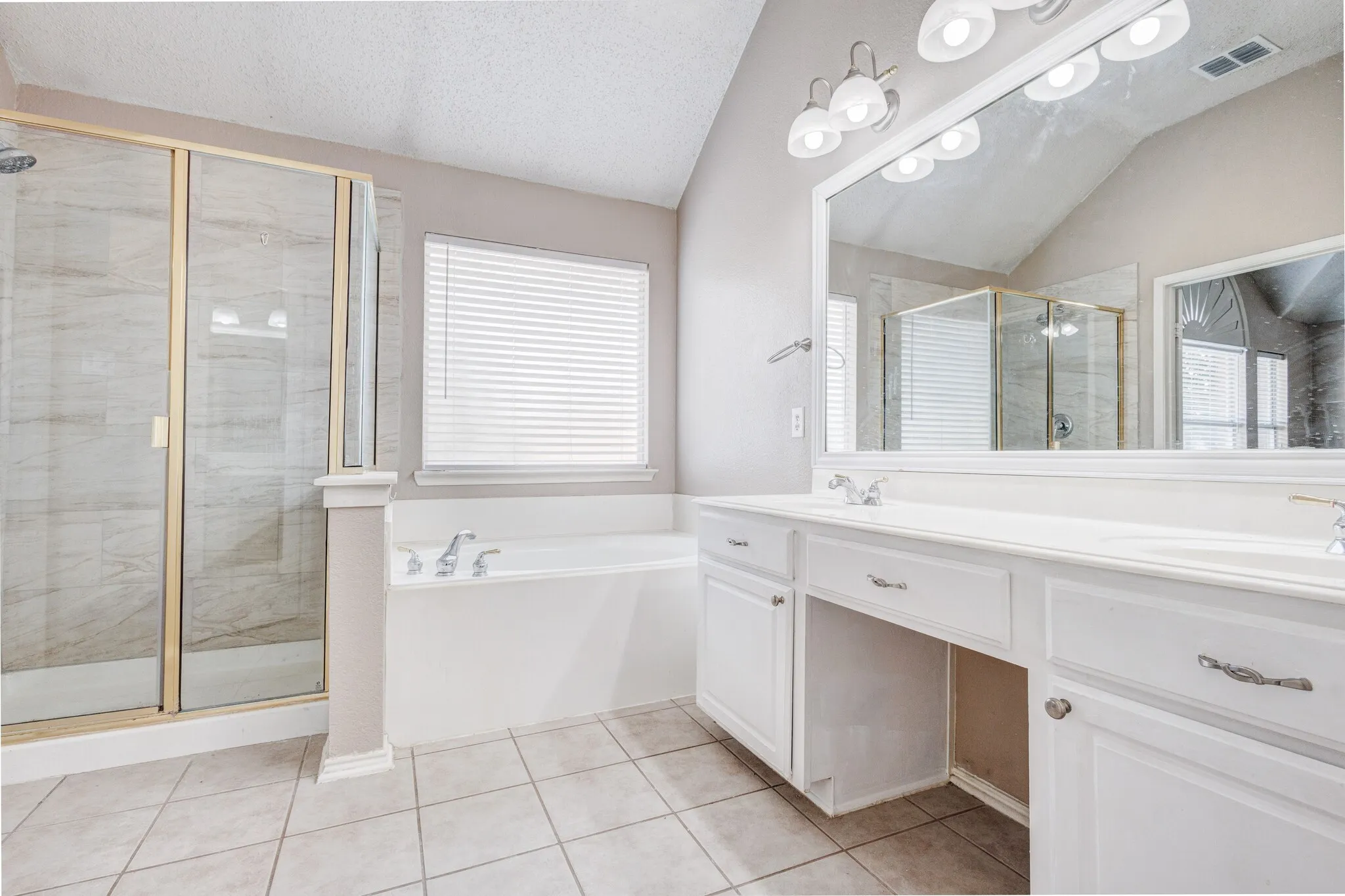 Bathroom featuring a dual vanity with white cabinetry, a built-in soaking tub, a glass-enclosed shower, and tile flooring