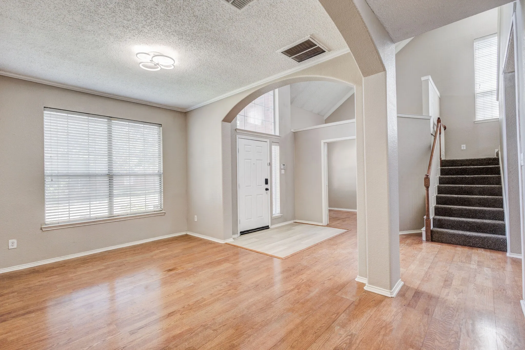 Entryway featuring wood-finish flooring, a carpeted staircase with wood handrails, and an arched doorway