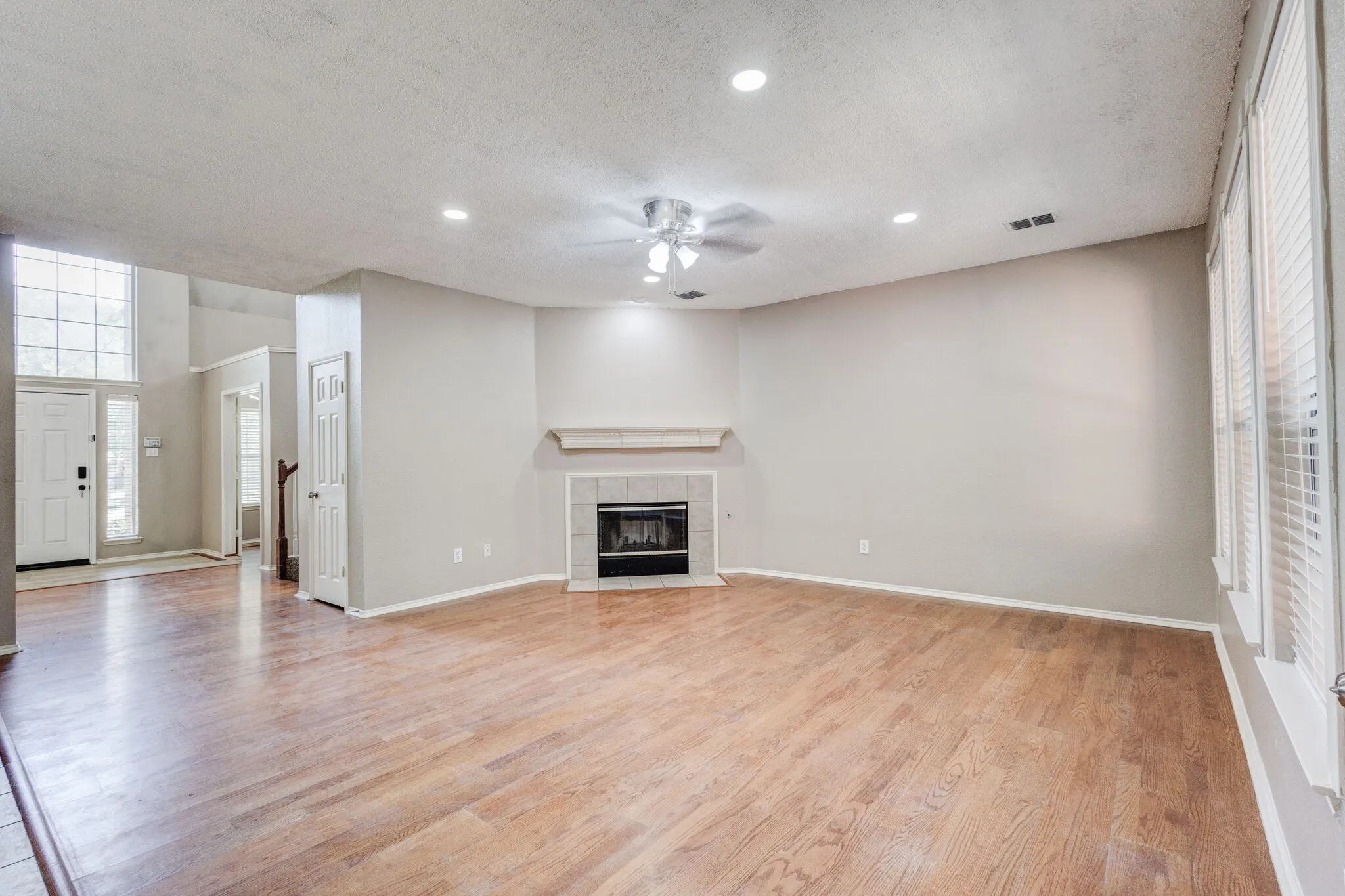 Spacious living area featuring wood-finish flooring, a tiled fireplace with mantel, and recessed lighting