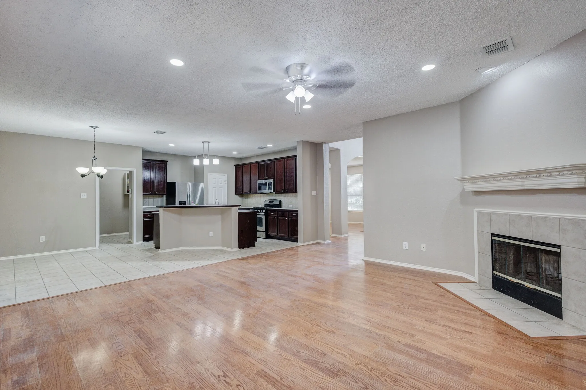 Spacious living area featuring wood-finish flooring, a tiled fireplace with a decorative mantel, and recessed lighting