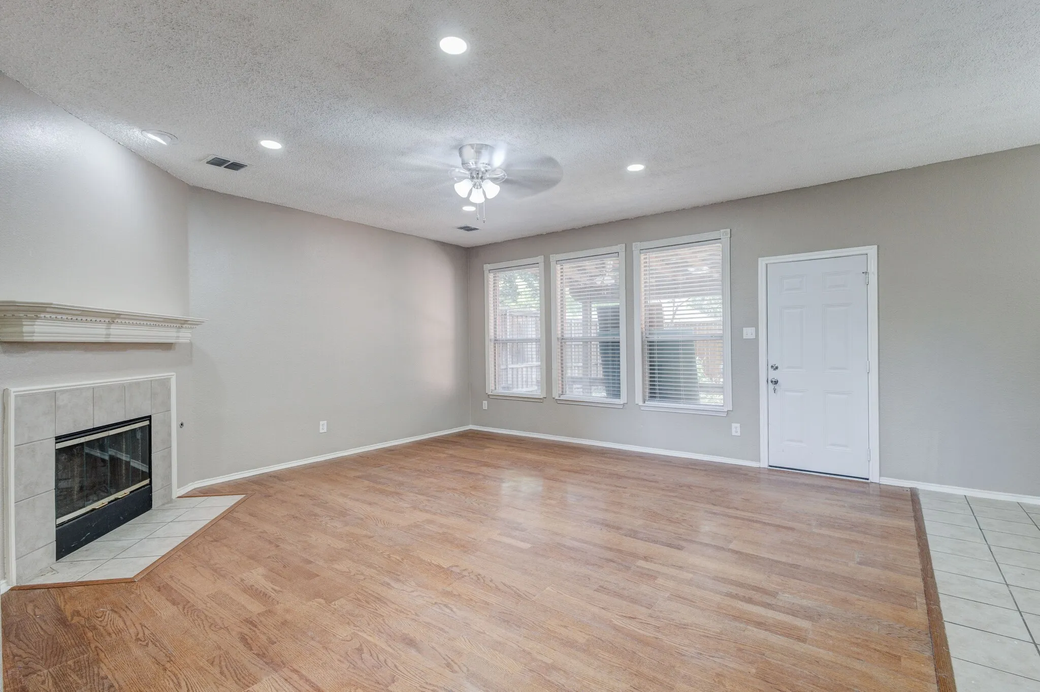 Spacious living area featuring wood-finish flooring, a tiled fireplace with a mantel, and recessed ceiling lighting